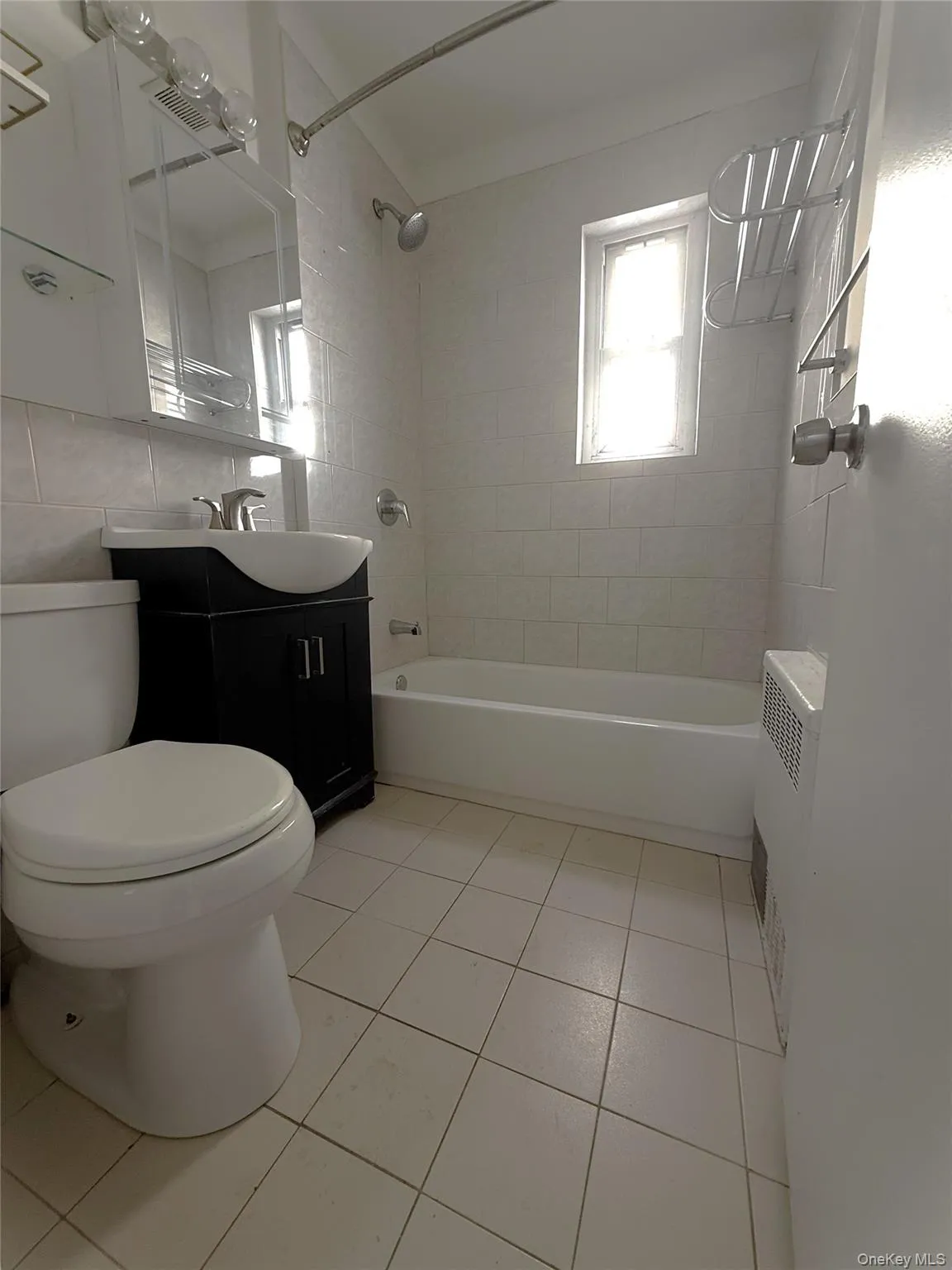 Full bath featuring tub / shower combination, vanity, light tile patterned floors, and tile walls Full bath featuring tub / shower combination, vanity, light tile patterned floors, and tile walls