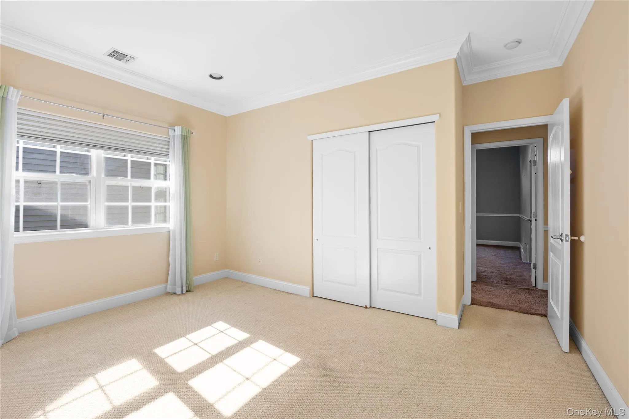 Unfurnished bedroom featuring light colored carpet, ornamental molding, and a closet Unfurnished bedroom featuring light colored carpet, ornamental molding, and a closet