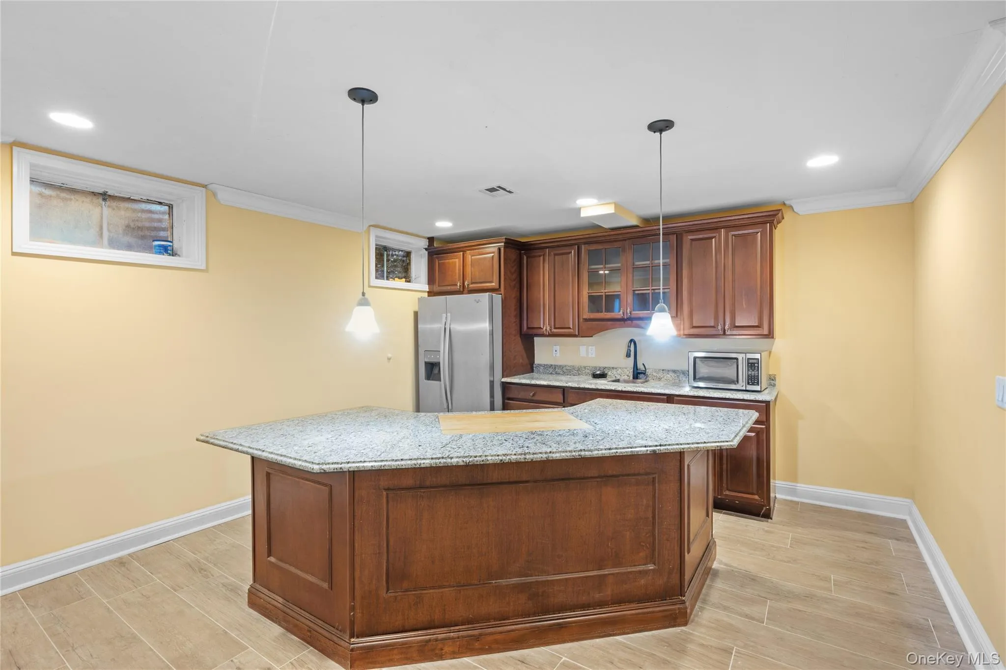 Kitchen featuring wood finish floors, crown molding, light stone countertops, appliances with stainless steel finishes, and brown cabinets Kitchen featuring wood finish floors, crown molding, light stone countertops, appliances with stainless steel finishes, and brown cabinets