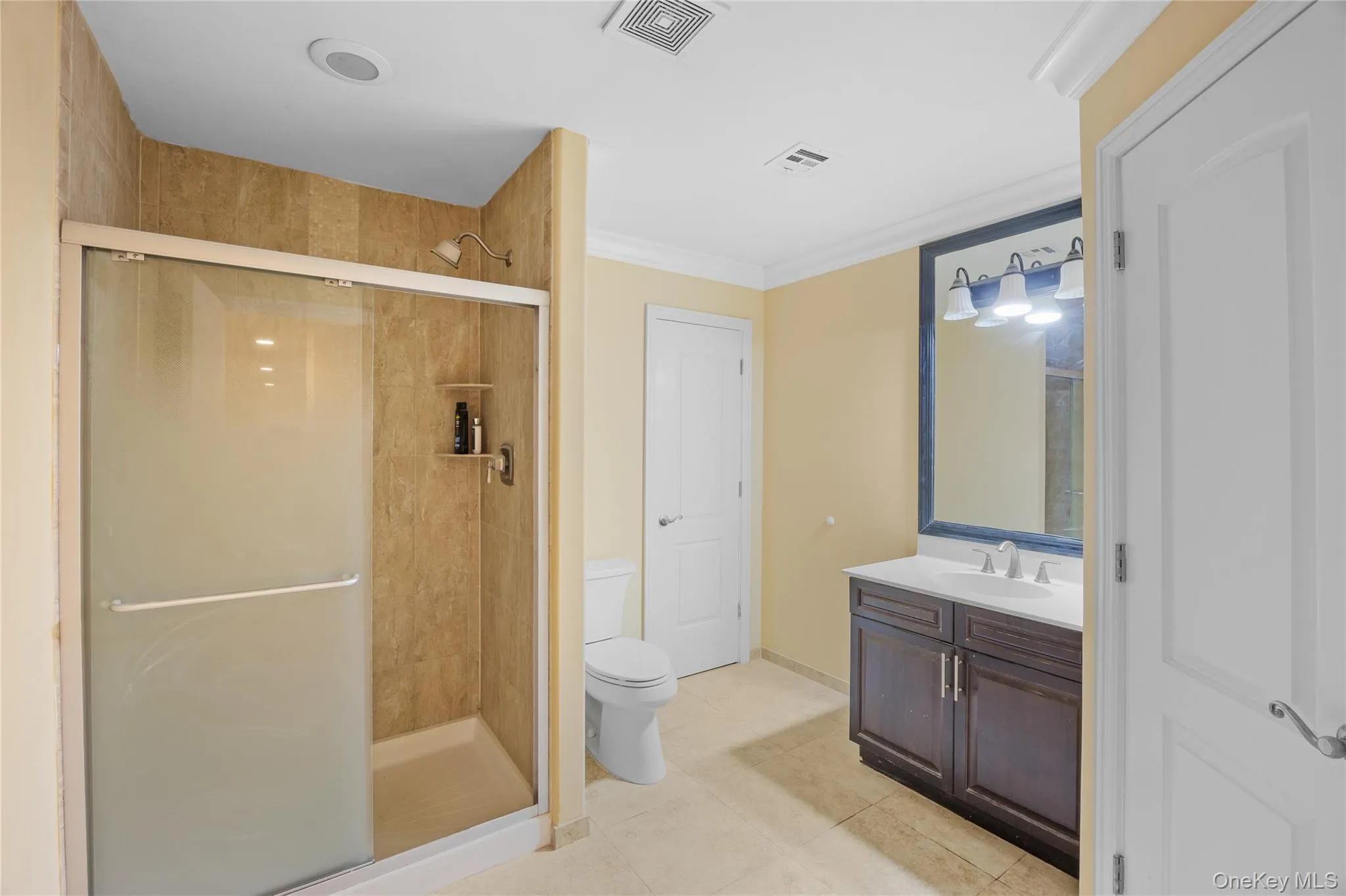 Bathroom with a shower stall, vanity, light tile patterned floors, and ornamental molding Bathroom with a shower stall, vanity, light tile patterned floors, and ornamental molding
