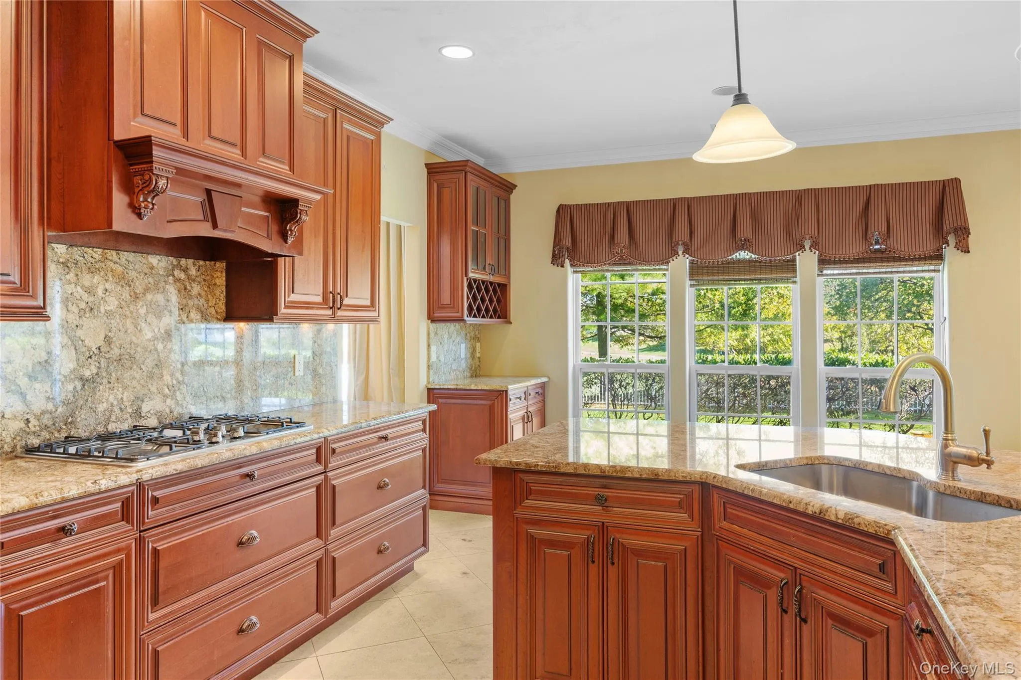 Kitchen with hanging light fixtures, decorative backsplash, light stone countertops, brown cabinets, and ornamental molding Kitchen with hanging light fixtures, decorative backsplash, light stone countertops, brown cabinets, and ornamental molding