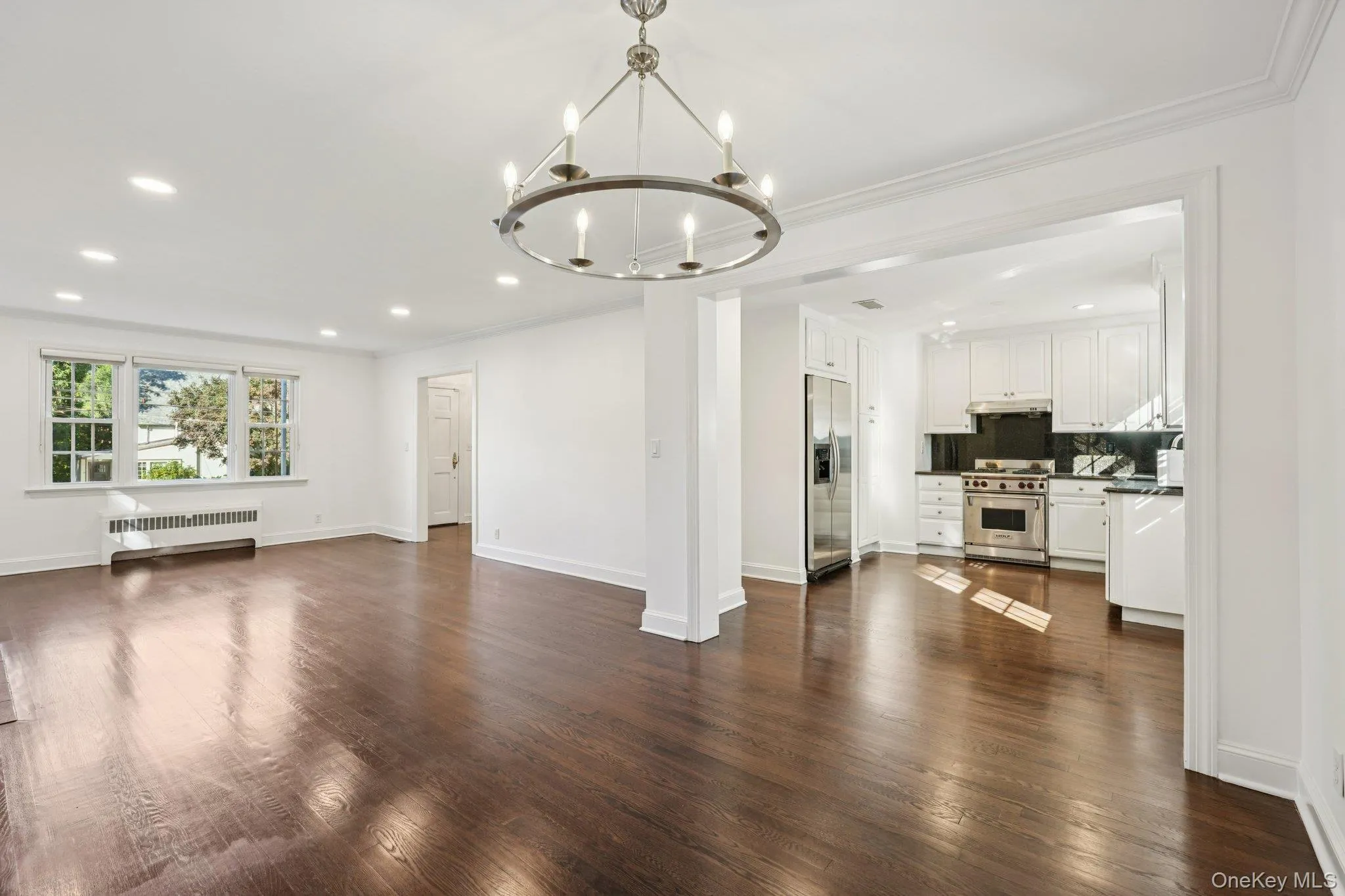 Unfurnished living room with recessed lighting, dark wood-style flooring, radiator heating unit, a chandelier, and crown molding Unfurnished living room with recessed lighting, dark wood-style flooring, radiator heating unit, a chandelier, and crown molding