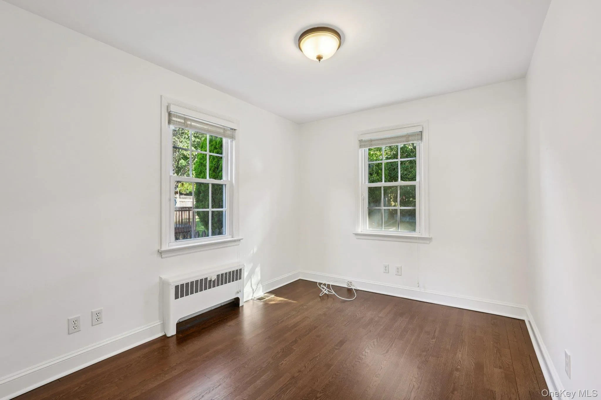 Unfurnished room featuring radiator and dark wood-style floors Unfurnished room featuring radiator and dark wood-style floors