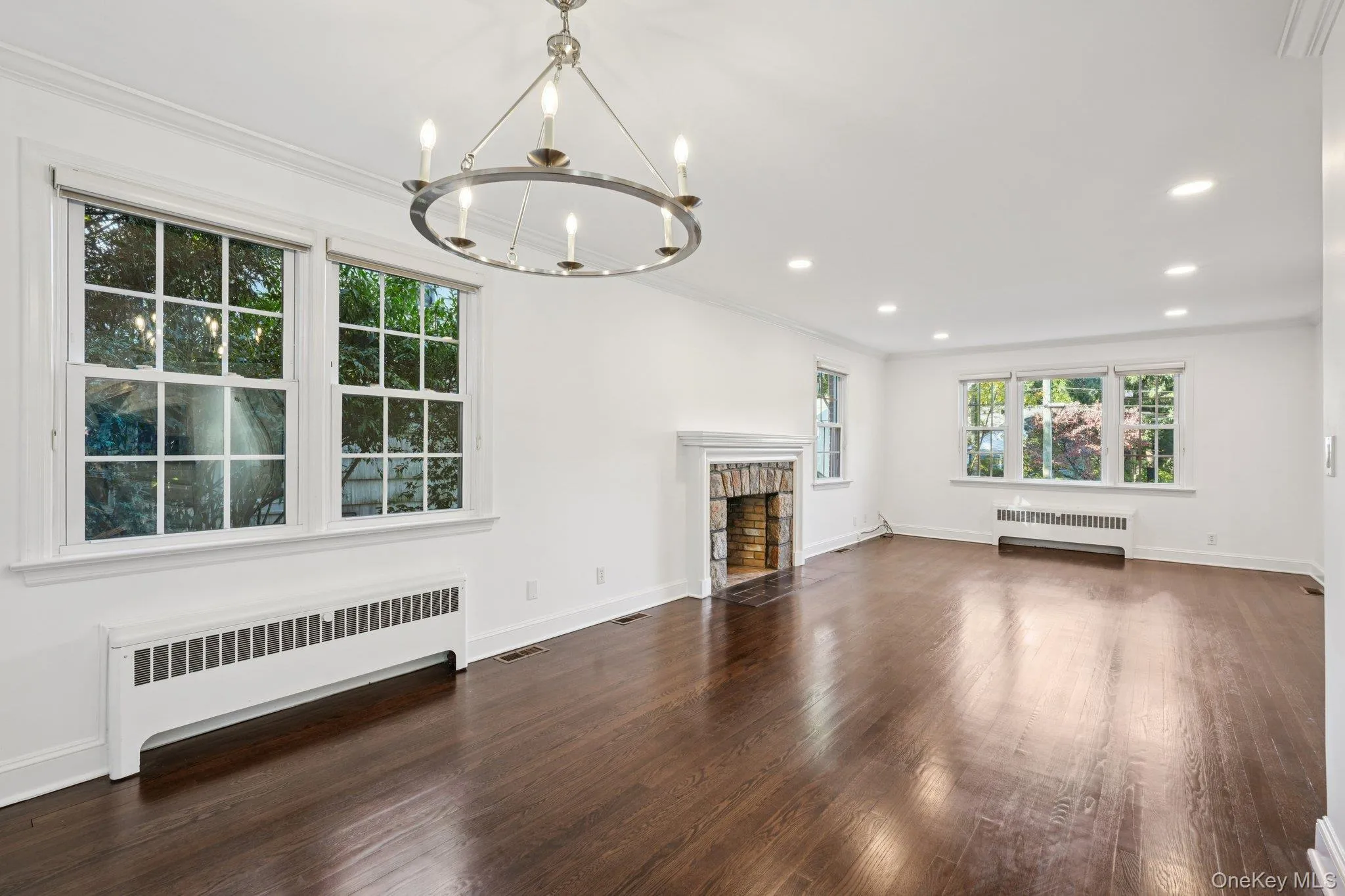 Unfurnished living room featuring radiator, dark wood-type flooring, crown molding, a fireplace with flush hearth, and recessed lighting Unfurnished living room featuring radiator, dark wood-type flooring, crown molding, a fireplace with flush hearth, and recessed lighting