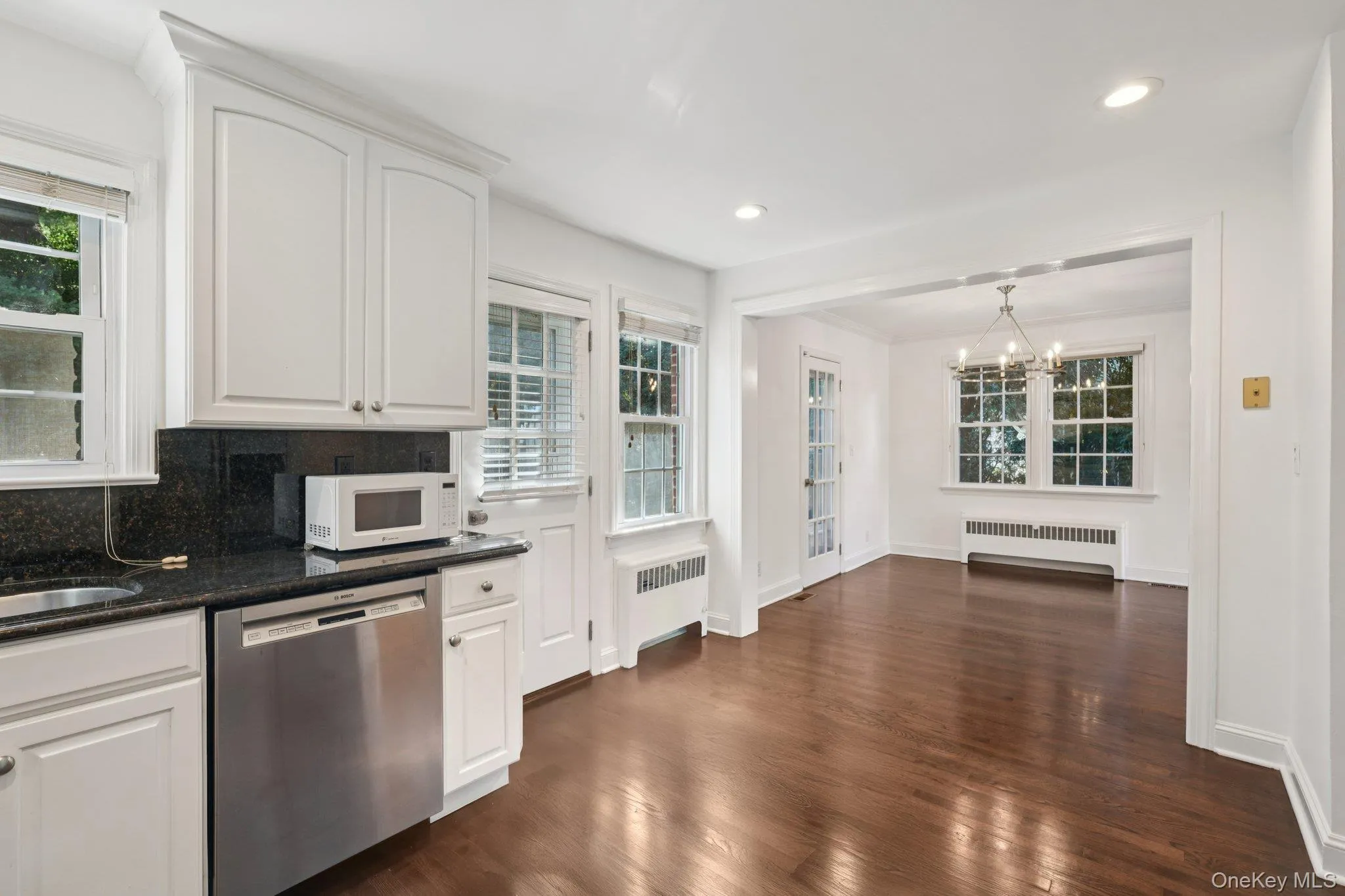 Kitchen featuring white cabinetry, stainless steel dishwasher, radiator heating unit, dark wood-style flooring, and recessed lighting Kitchen featuring white cabinetry, stainless steel dishwasher, radiator heating unit, dark wood-style flooring, and recessed lighting