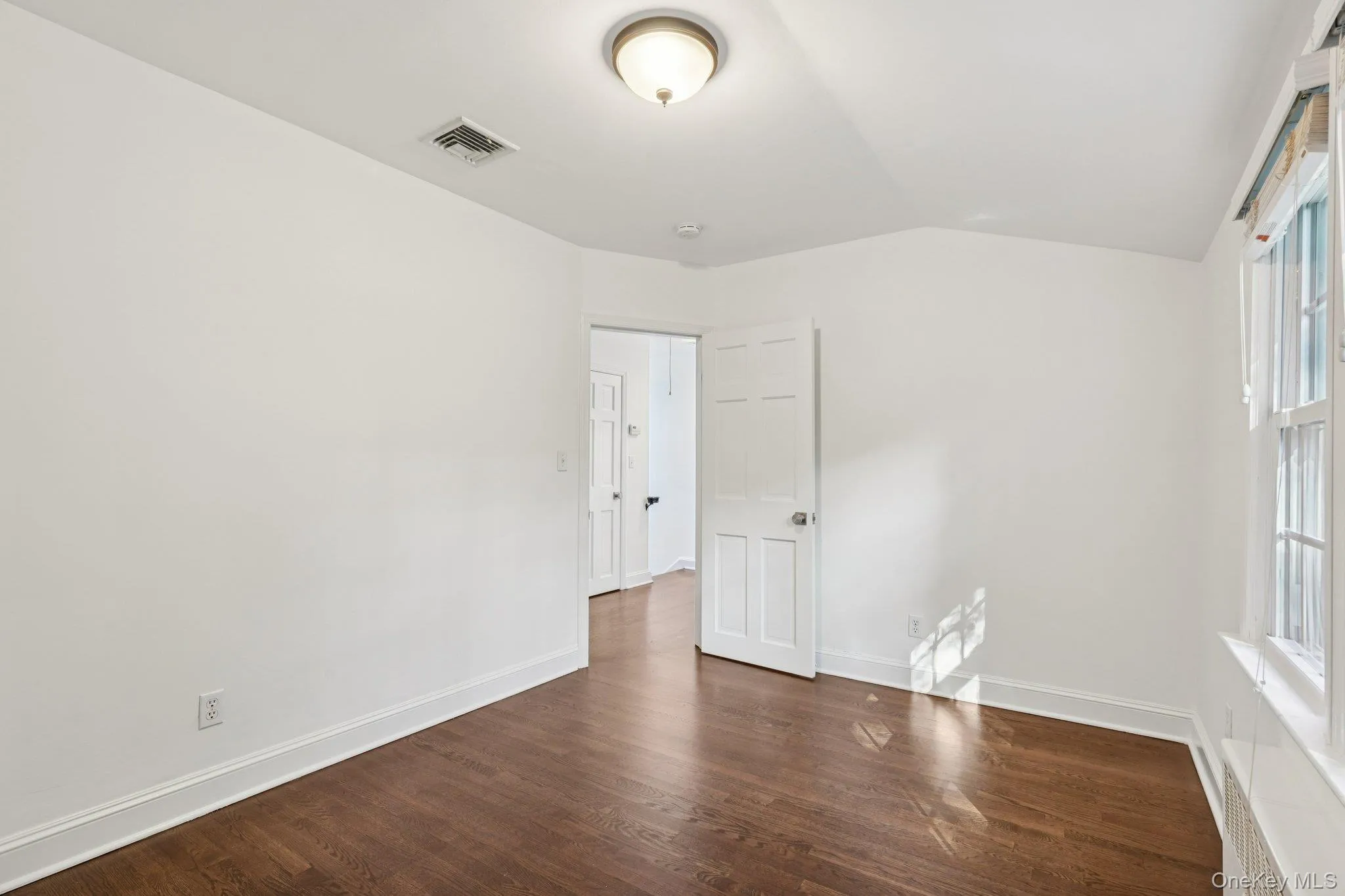 Unfurnished room featuring dark wood finished floors, lofted ceiling, and radiator Unfurnished room featuring dark wood finished floors, lofted ceiling, and radiator