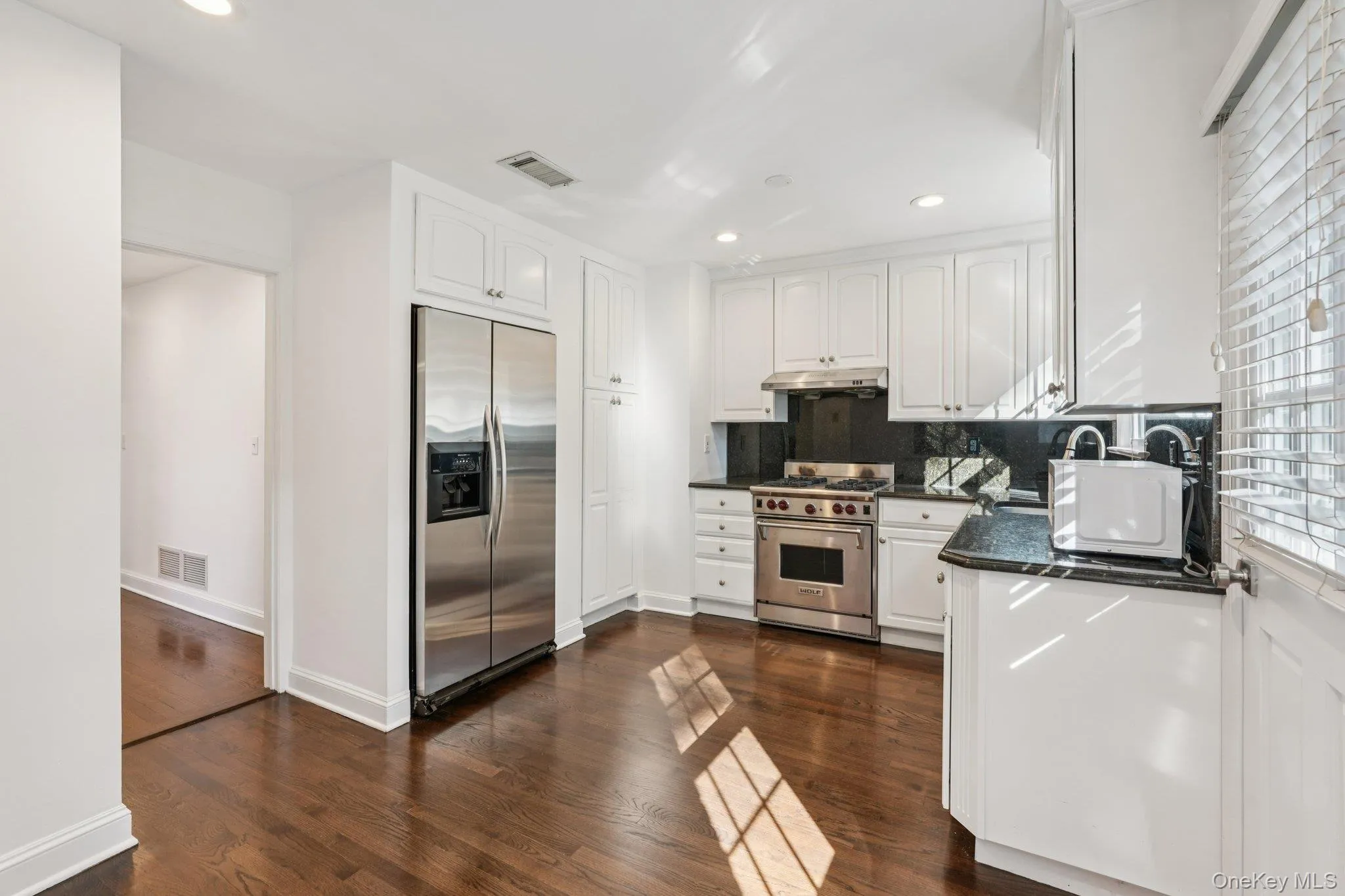 Kitchen with stainless steel appliances, white cabinetry, recessed lighting, dark stone counters, and dark wood finished floors Kitchen with stainless steel appliances, white cabinetry, recessed lighting, dark stone counters, and dark wood finished floors