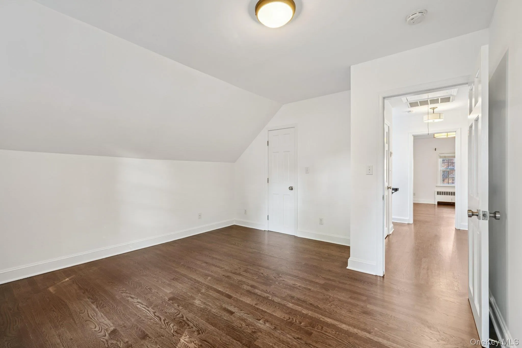Bonus room with vaulted ceiling, dark wood finished floors, attic access, and radiator Bonus room with vaulted ceiling, dark wood finished floors, attic access, and radiator