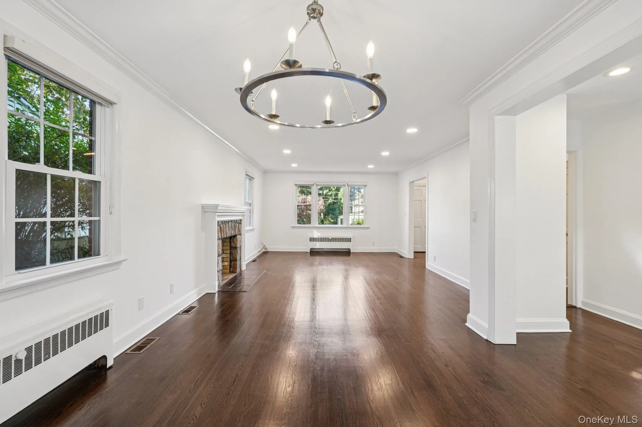 Unfurnished living room featuring radiator heating unit, crown molding, dark wood-type flooring, a chandelier, and a fireplace with flush hearth Unfurnished living room featuring radiator heating unit, crown molding, dark wood-type flooring, a chandelier, and a fireplace with flush hearth