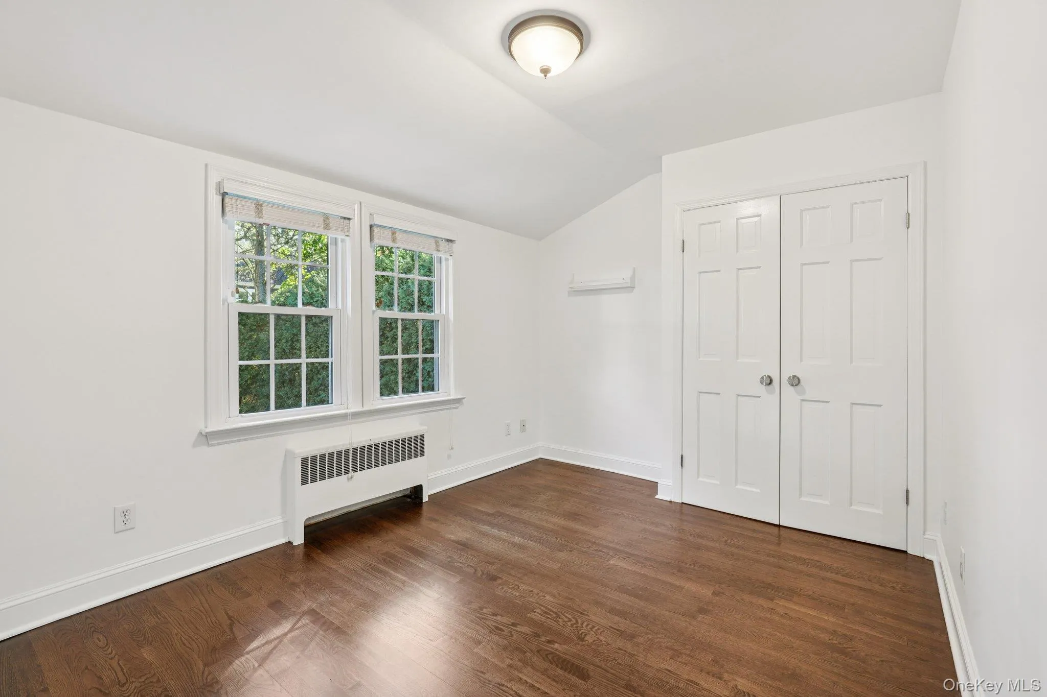 Unfurnished bedroom featuring radiator heating unit, lofted ceiling, dark wood-style flooring, and a closet Unfurnished bedroom featuring radiator heating unit, lofted ceiling, dark wood-style flooring, and a closet