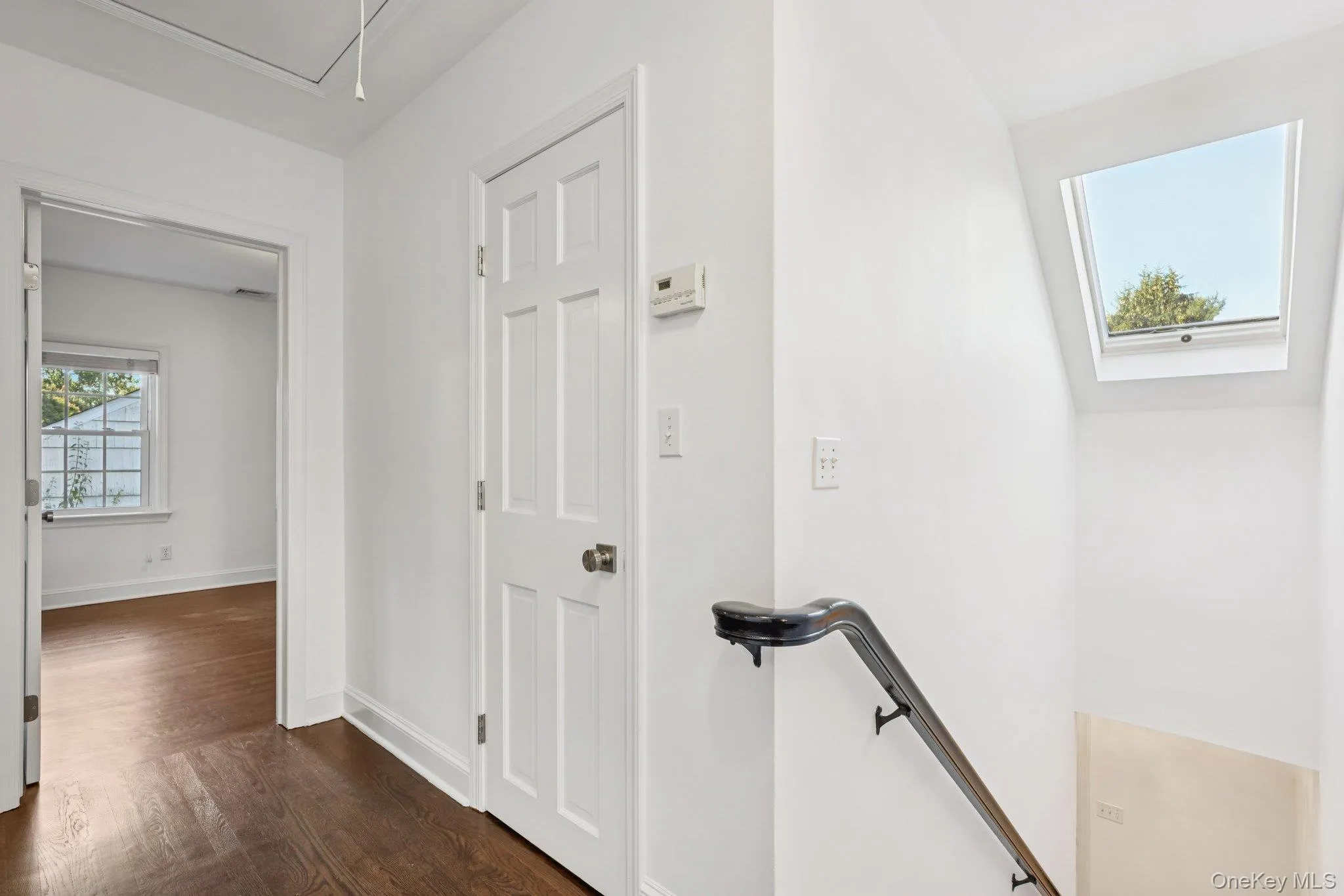 Hallway with an upstairs landing, attic access, and dark wood-style flooring Hallway with an upstairs landing, attic access, and dark wood-style flooring