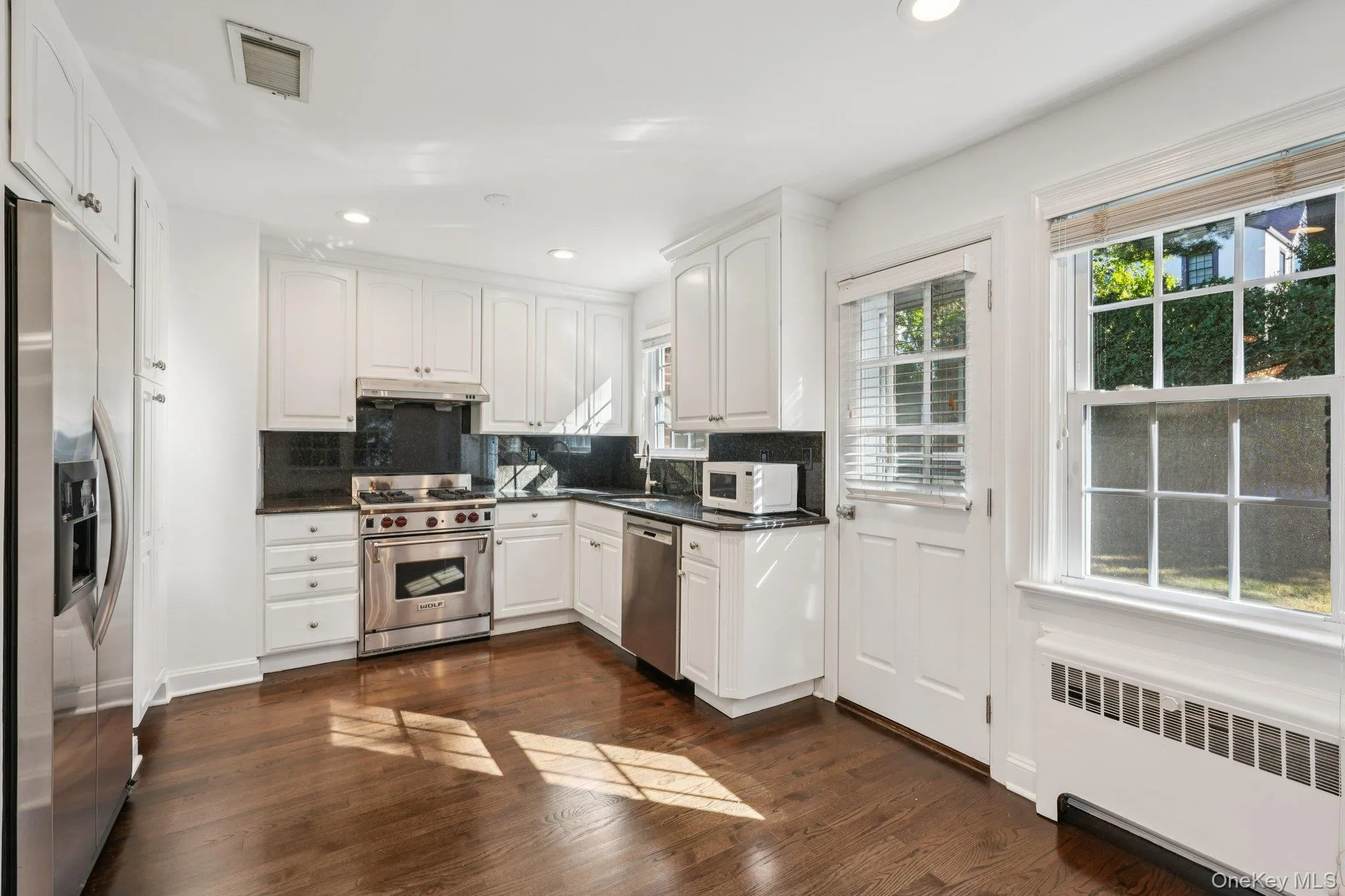 Kitchen featuring radiator heating unit, white cabinets, appliances with stainless steel finishes, dark wood-style floors, and recessed lighting Kitchen featuring radiator heating unit, white cabinets, appliances with stainless steel finishes, dark wood-style floors, and recessed lighting