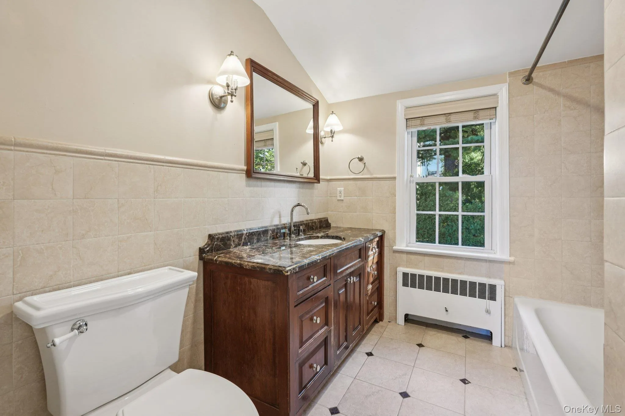 Full bath featuring radiator heating unit, tile walls, vanity, light tile patterned flooring, and vaulted ceiling Full bath featuring radiator heating unit, tile walls, vanity, light tile patterned flooring, and vaulted ceiling