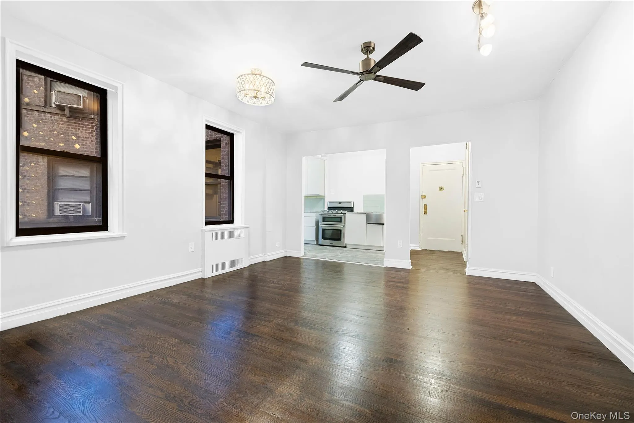 Unfurnished living room with dark wood-style flooring, a ceiling fan, radiator heating unit, and a chandelier Unfurnished living room with dark wood-style flooring, a ceiling fan, radiator heating unit, and a chandelier