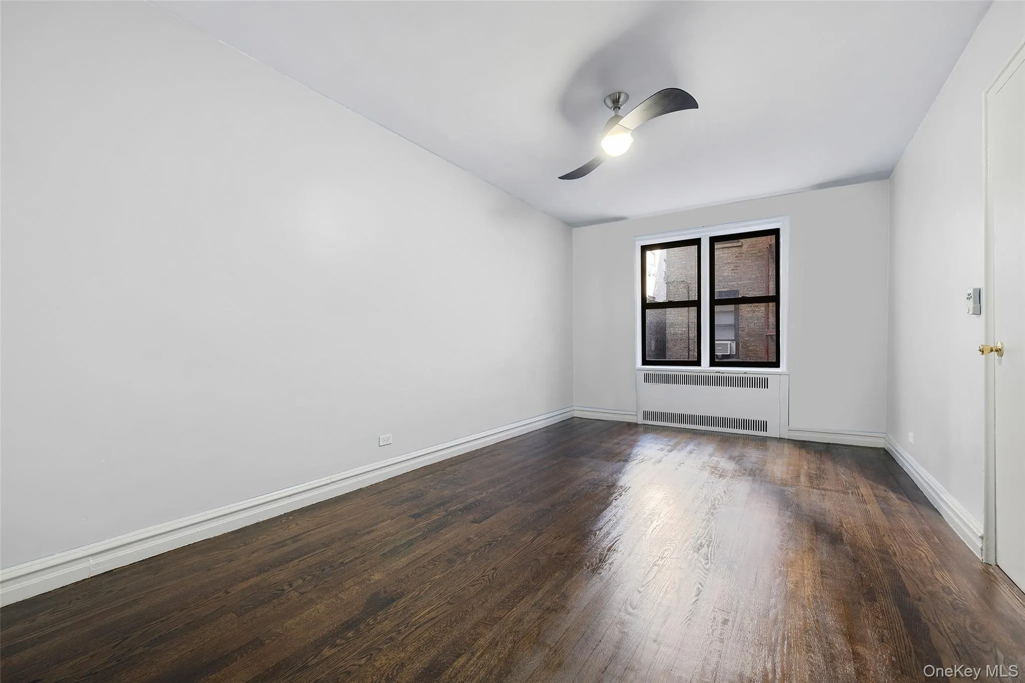 Empty room featuring dark wood finished floors, radiator heating unit, and ceiling fan Empty room featuring dark wood finished floors, radiator heating unit, and ceiling fan