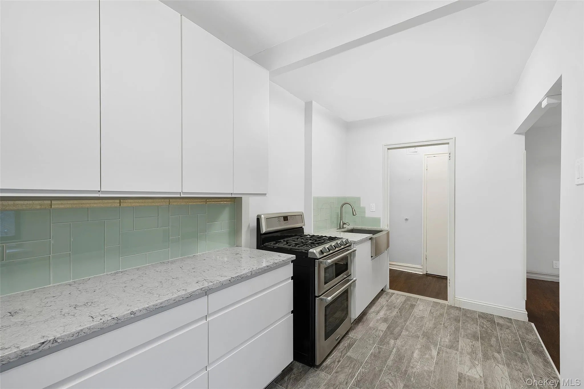 Kitchen featuring white cabinetry, double oven range, backsplash, light wood-style floors, and light stone countertops Kitchen featuring white cabinetry, double oven range, backsplash, light wood-style floors, and light stone countertops