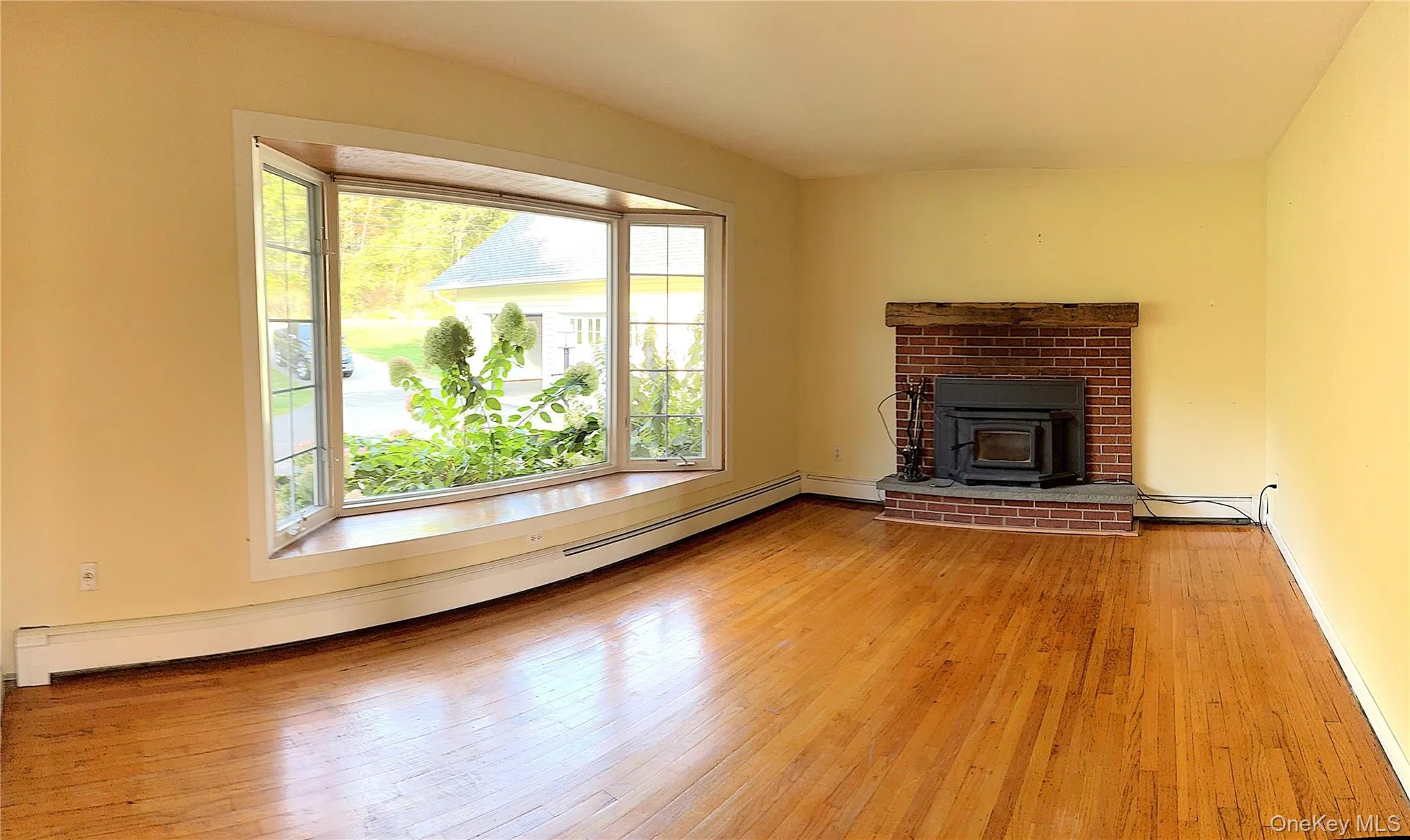 Unfurnished living room featuring a baseboard radiator, light wood-style flooring, and a wood stove Unfurnished living room featuring a baseboard radiator, light wood-style flooring, and a wood stove