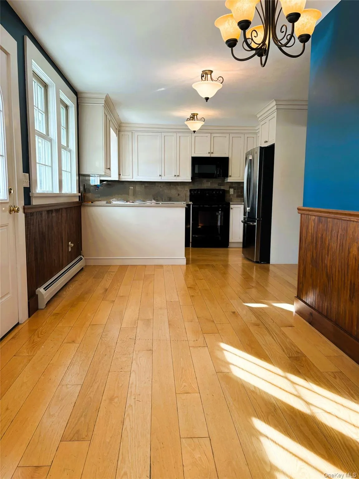 Kitchen with black appliances, light wood finished floors, white cabinetry, baseboard heating, and tasteful backsplash Kitchen with black appliances, light wood finished floors, white cabinetry, baseboard heating, and tasteful backsplash