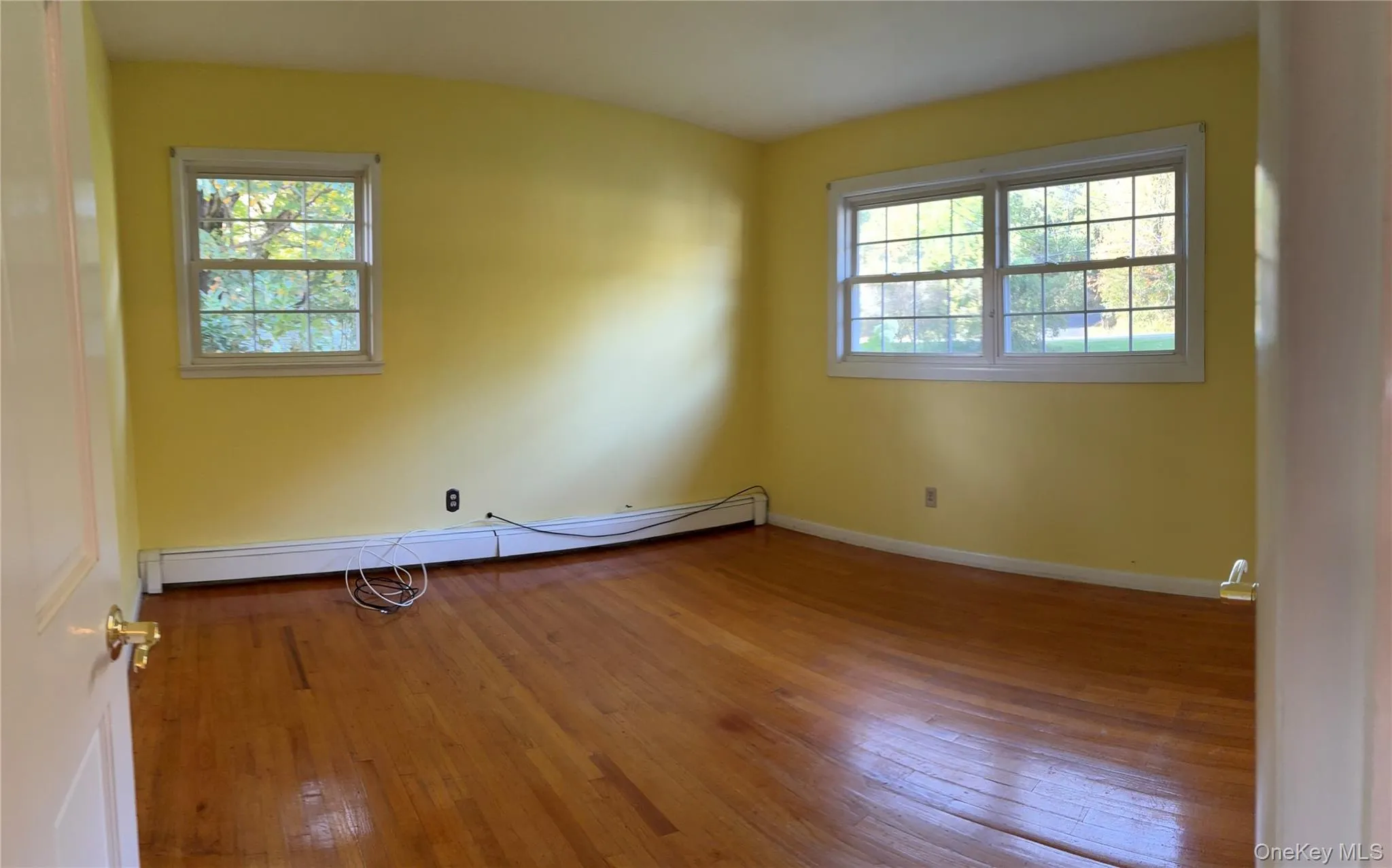 Unfurnished room with hardwood / wood-style floors and baseboard heating Unfurnished room with hardwood / wood-style floors and baseboard heating