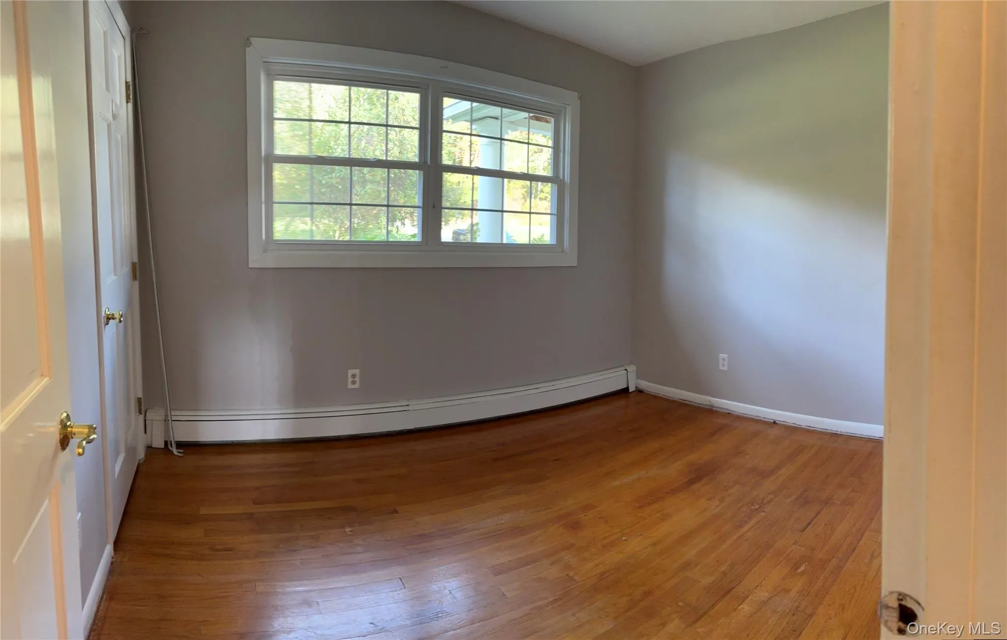 Empty room featuring a baseboard heating unit and hardwood / wood-style floors Empty room featuring a baseboard heating unit and hardwood / wood-style floors