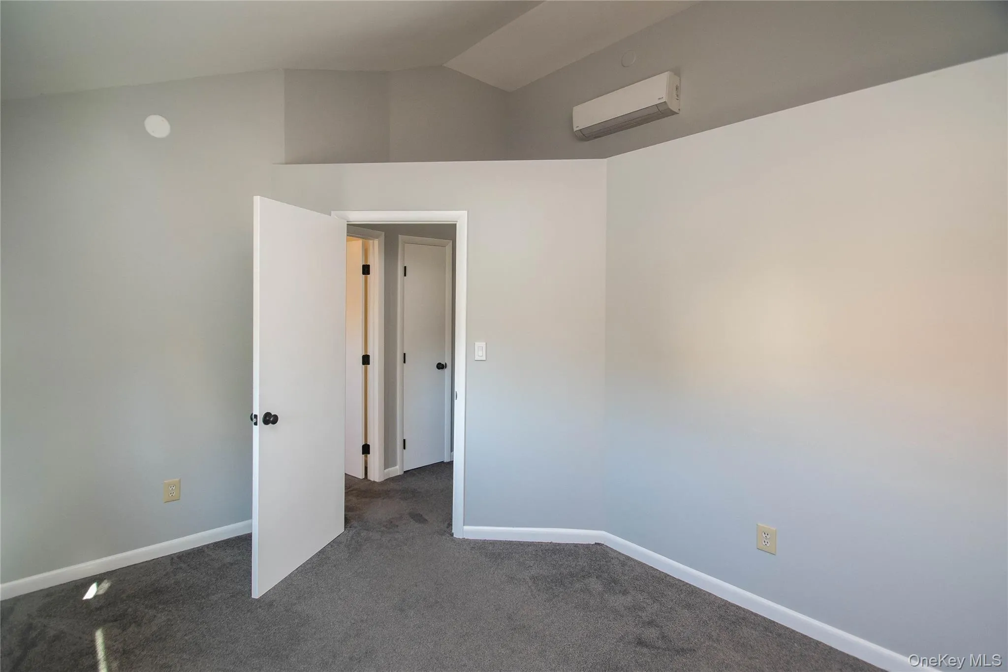 Spare room with dark carpet, lofted ceiling, and an AC wall unit Spare room with dark carpet, lofted ceiling, and an AC wall unit
