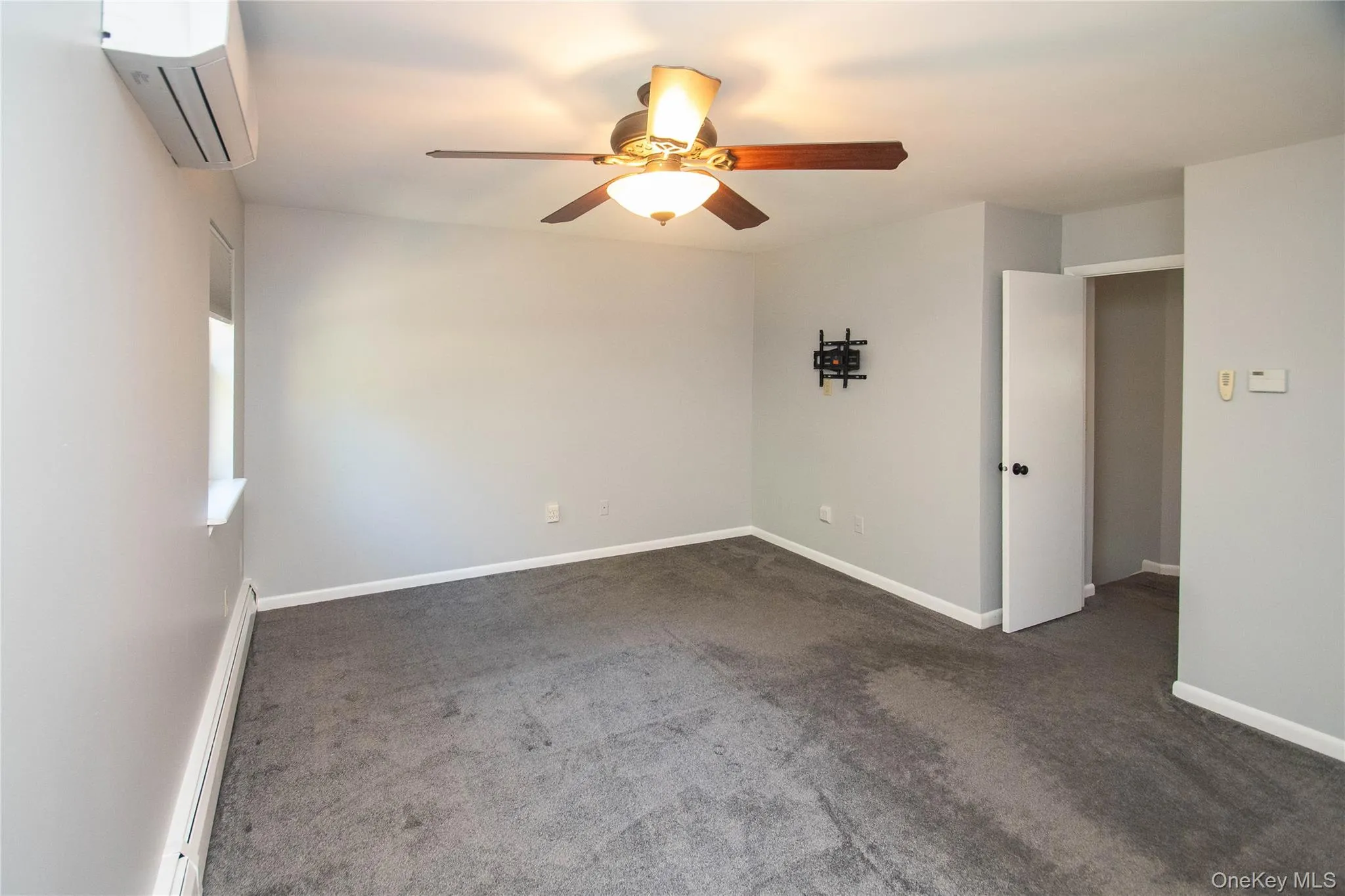 Unfurnished room featuring dark carpet, baseboard heating, a wall unit AC, and a ceiling fan Unfurnished room featuring dark carpet, baseboard heating, a wall unit AC, and a ceiling fan