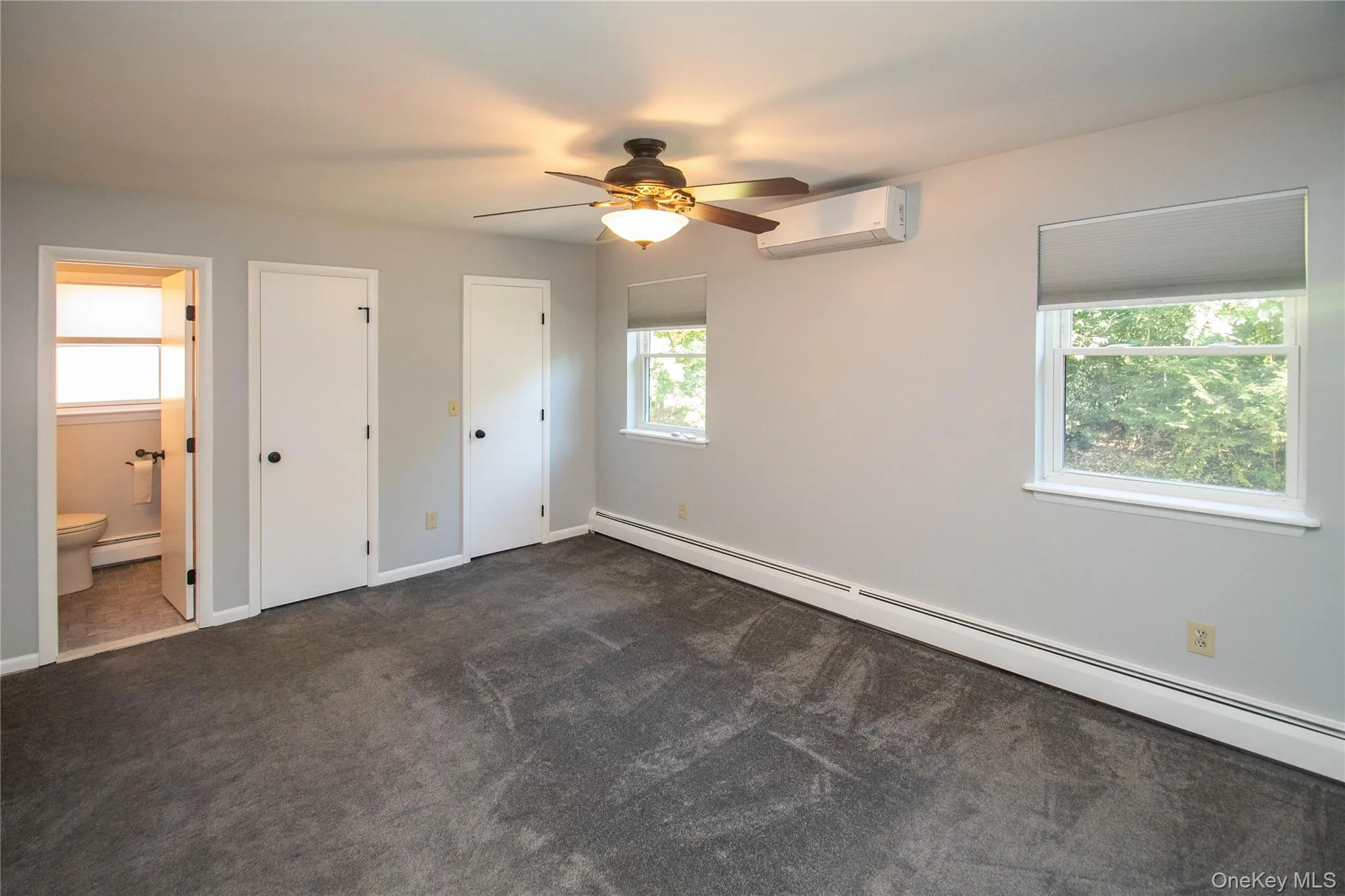 Unfurnished bedroom with a baseboard heating unit, dark carpet, an AC wall unit, multiple closets, and ceiling fan Unfurnished bedroom with a baseboard heating unit, dark carpet, an AC wall unit, multiple closets, and ceiling fan