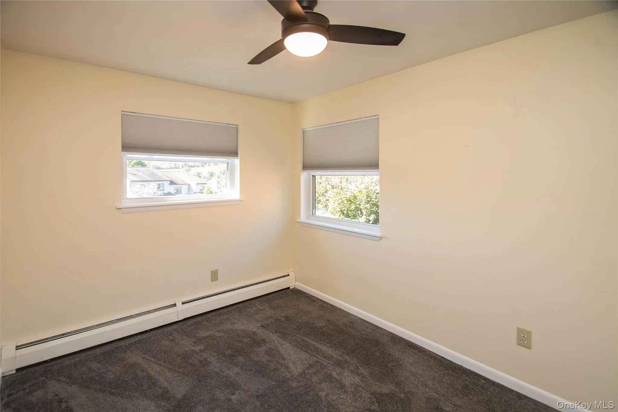 Empty room featuring baseboard heating, dark colored carpet, and ceiling fan Empty room featuring baseboard heating, dark colored carpet, and ceiling fan