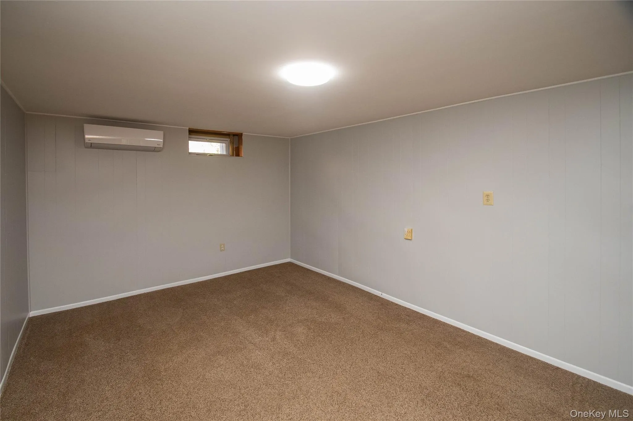 Below grade area featuring carpet, a wall mounted air conditioner, and wooden walls Below grade area featuring carpet, a wall mounted air conditioner, and wooden walls