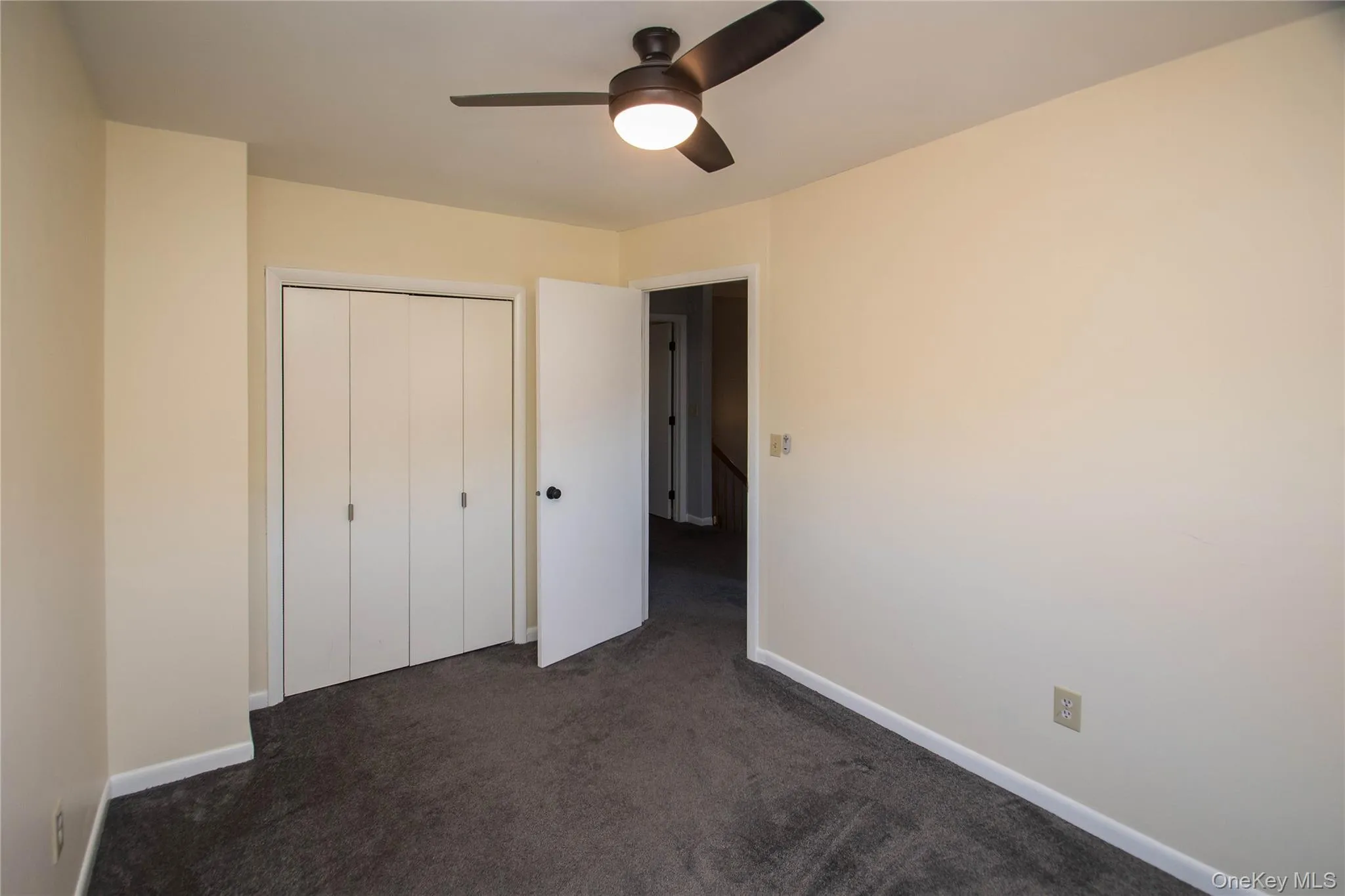 Unfurnished bedroom featuring dark colored carpet, a ceiling fan, and a closet Unfurnished bedroom featuring dark colored carpet, a ceiling fan, and a closet