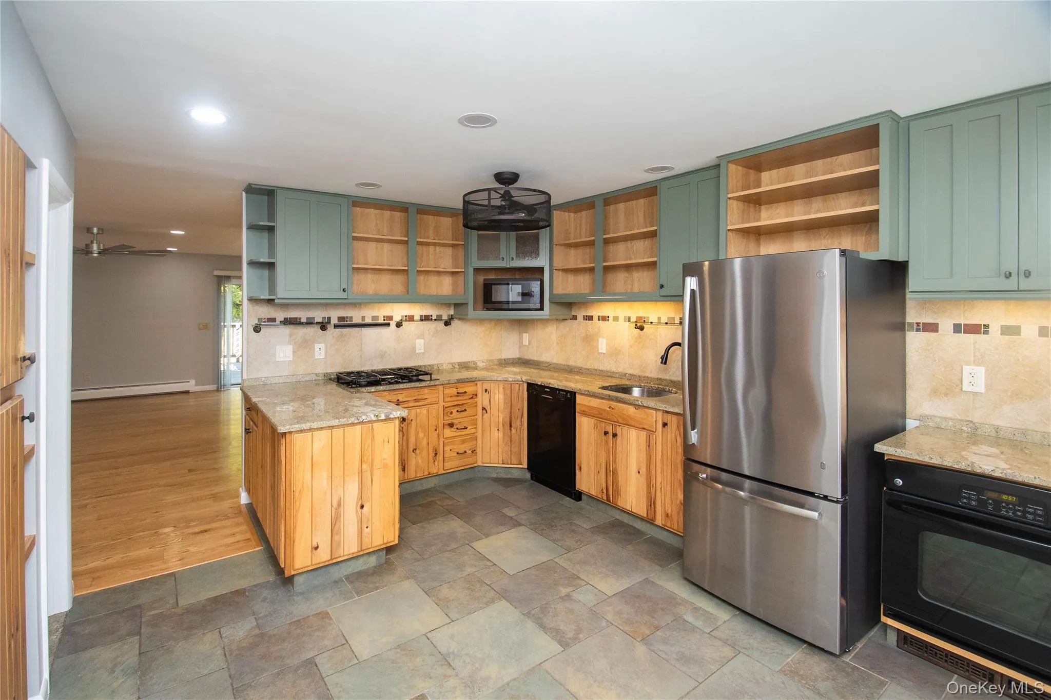 Kitchen featuring open shelves, green cabinetry, black appliances, a peninsula, and light stone counters Kitchen featuring open shelves, green cabinetry, black appliances, a peninsula, and light stone counters