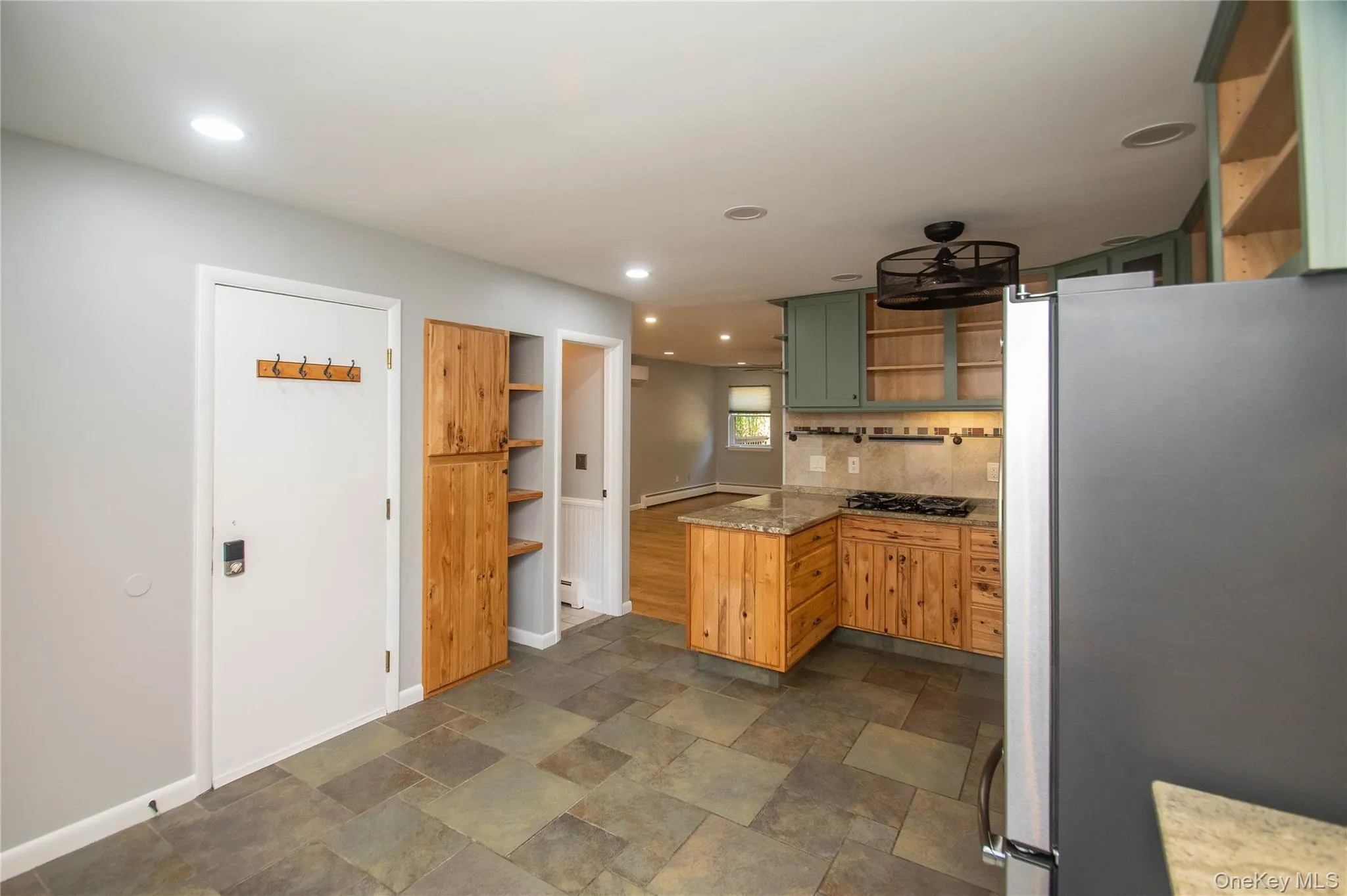 Kitchen with open shelves, freestanding refrigerator, green cabinets, a peninsula, and dark stone finish floors Kitchen with open shelves, freestanding refrigerator, green cabinets, a peninsula, and dark stone finish floors