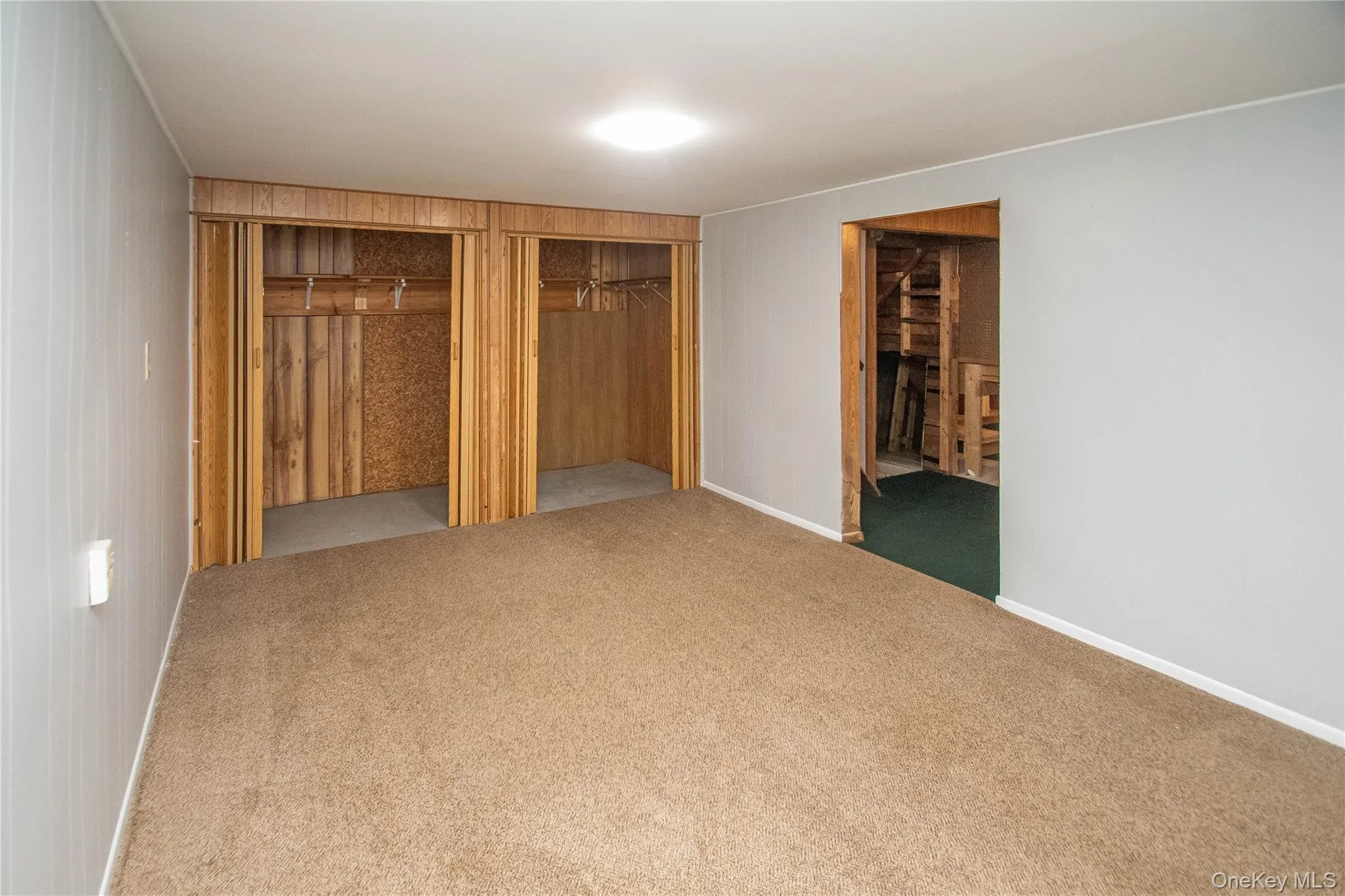 Unfurnished bedroom featuring two closets, carpet, and wood walls Unfurnished bedroom featuring two closets, carpet, and wood walls