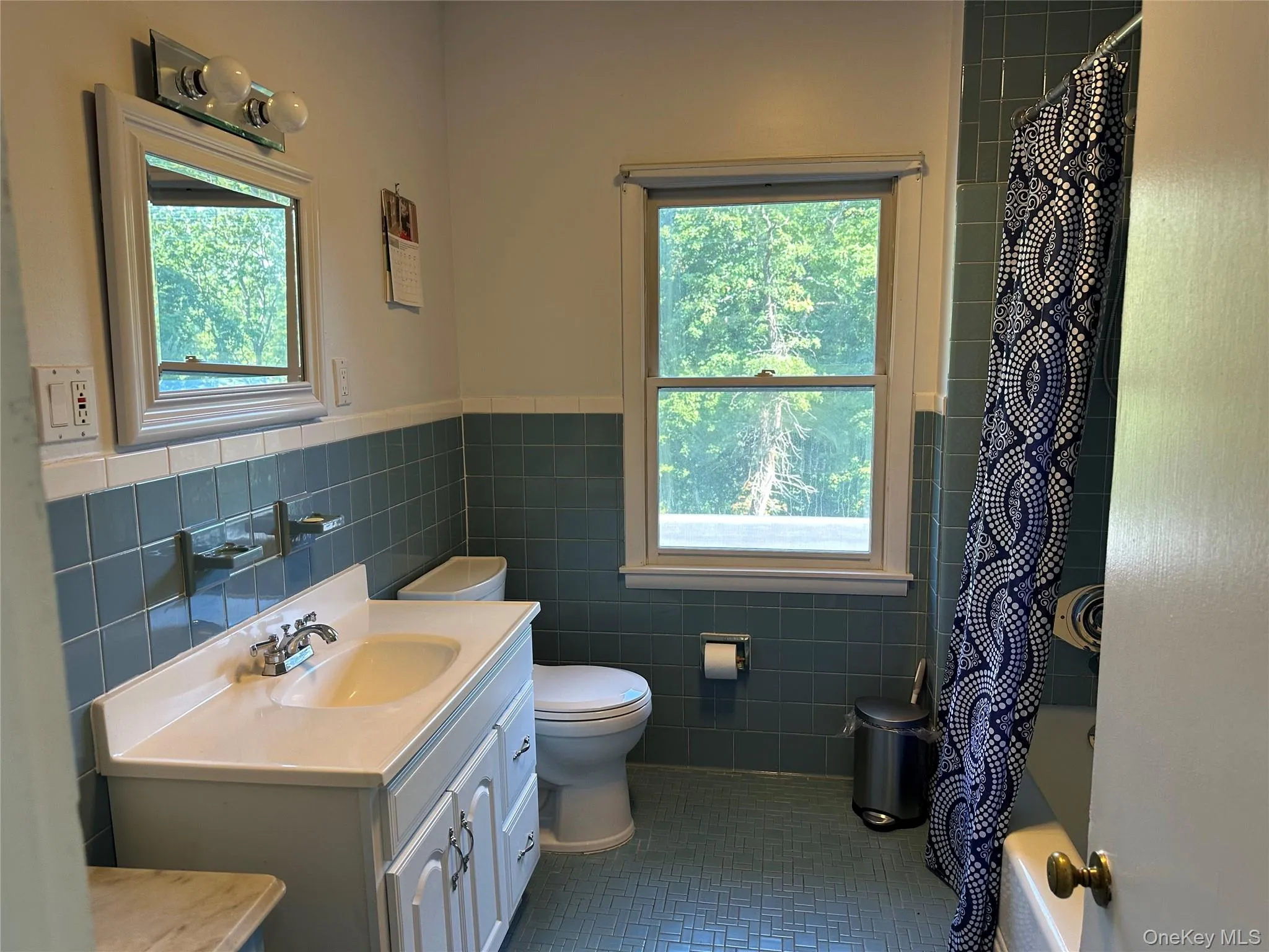 Full bath featuring vanity, tile walls, plenty of natural light, dark tile patterned floors, and shower / tub combo with curtain Full bath featuring vanity, tile walls, plenty of natural light, dark tile patterned floors, and shower / tub combo with curtain