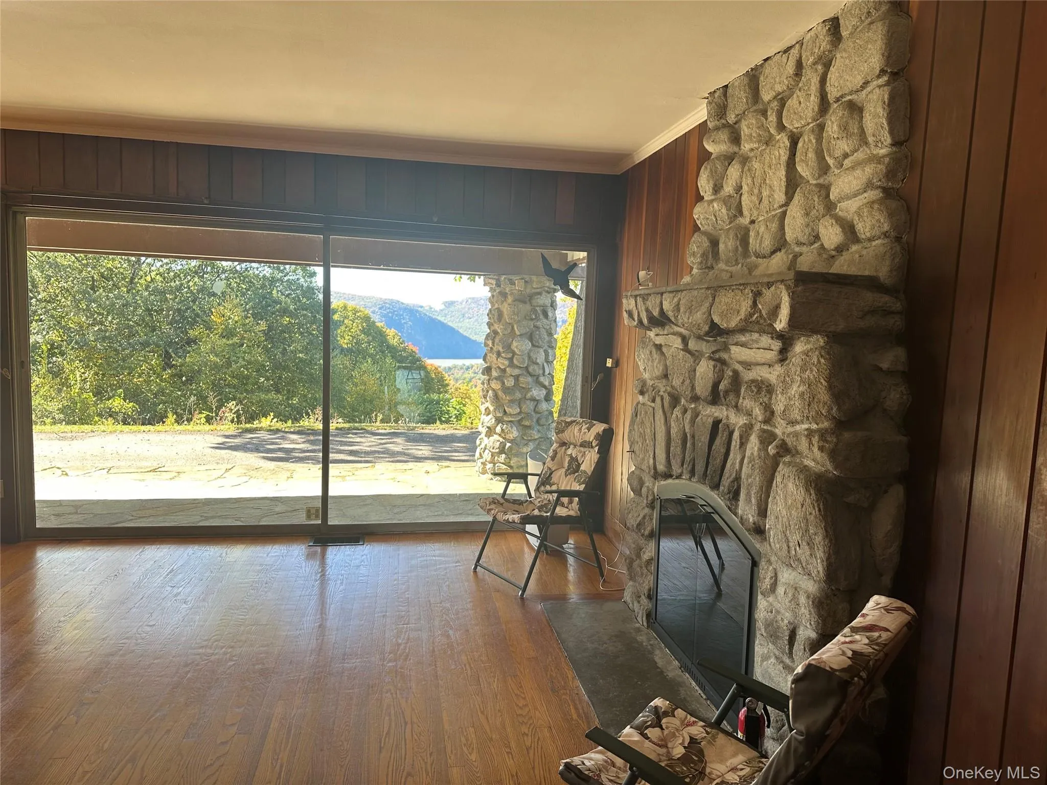 Living area featuring crown molding, wood finished floors, a stone fireplace, and wood walls Living area featuring crown molding, wood finished floors, a stone fireplace, and wood walls