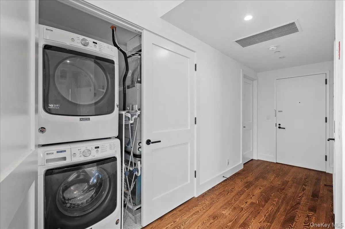 Laundry room with dark wood-style flooring and stacked washing machine and dryer Laundry room with dark wood-style flooring and stacked washing machine and dryer