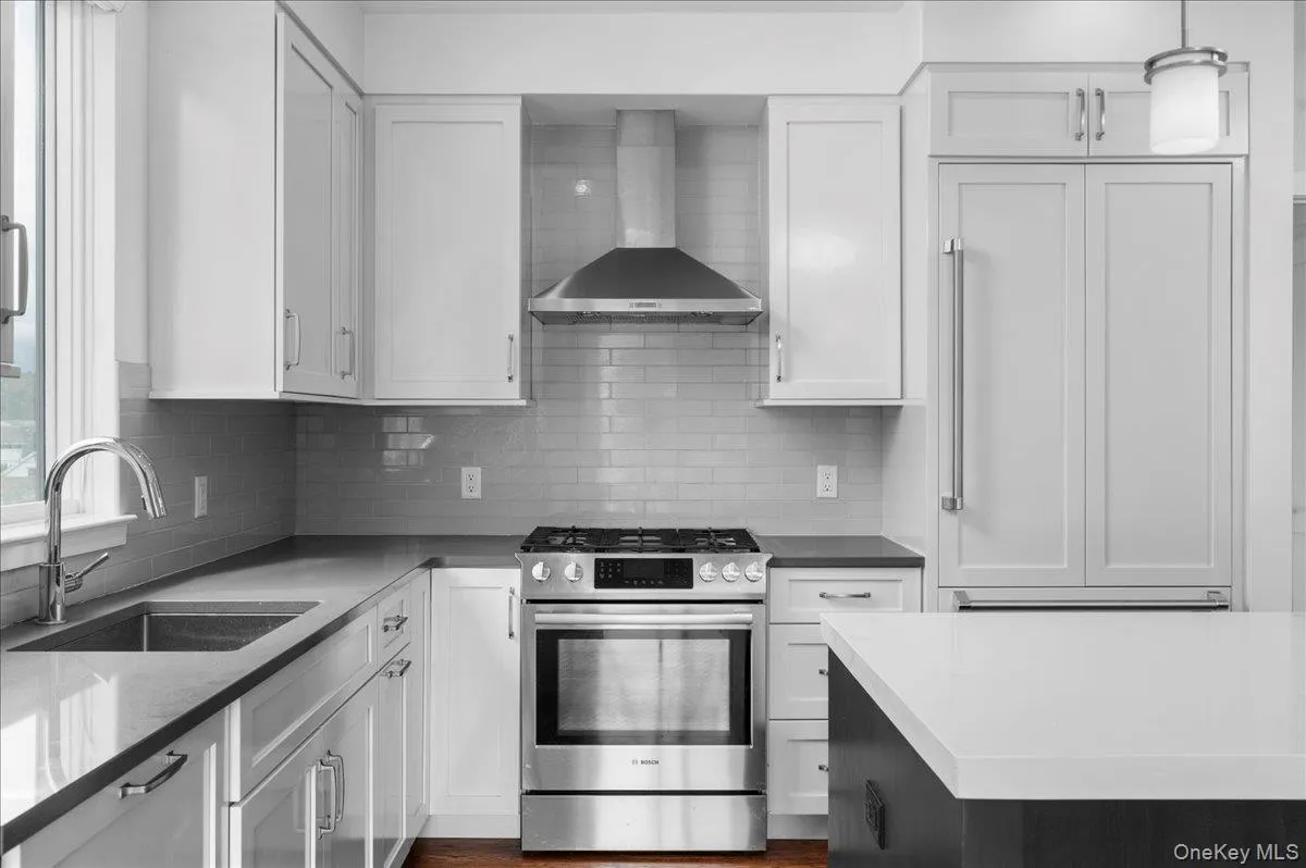 Kitchen featuring stainless steel gas stove, wall chimney range hood, and white cabinetry Kitchen featuring stainless steel gas stove, wall chimney range hood, and white cabinetry