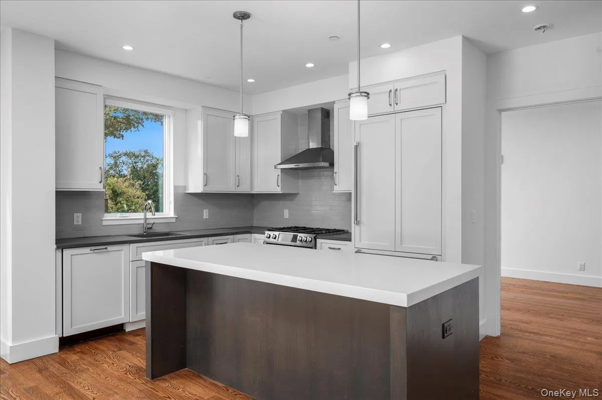 Kitchen featuring recessed lighting, tasteful backsplash, wall chimney range hood, dark wood-style flooring, and dark brown cabinetry Kitchen featuring recessed lighting, tasteful backsplash, wall chimney range hood, dark wood-style flooring, and dark brown cabinetry