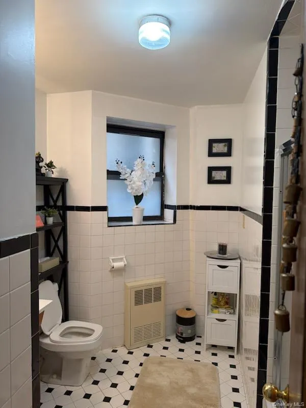 Bathroom with tile walls, wainscoting, radiator, and light tile patterned flooring Bathroom with tile walls, wainscoting, radiator, and light tile patterned flooring