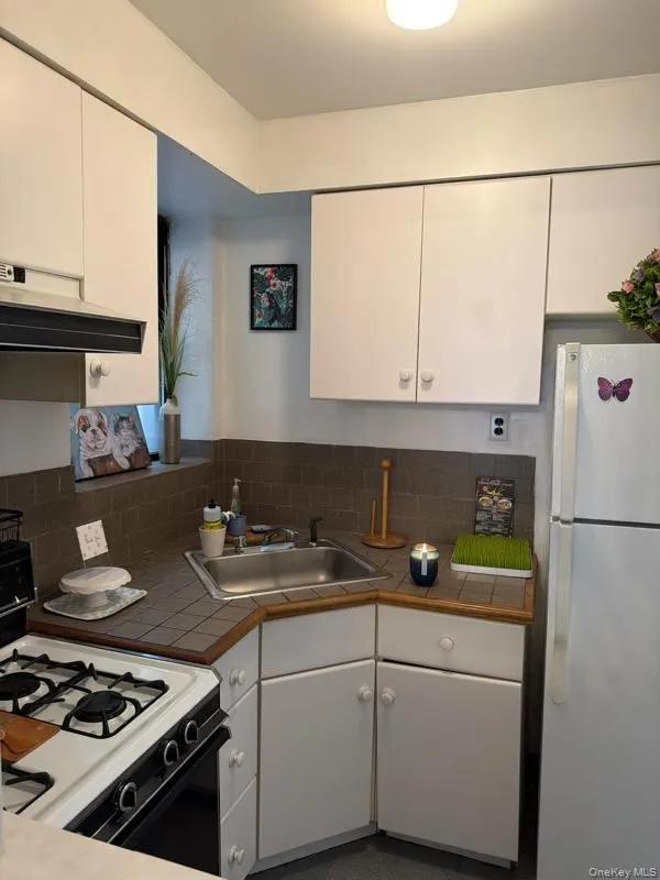 Kitchen featuring white appliances, white cabinetry, under cabinet range hood, and tile countertops Kitchen featuring white appliances, white cabinetry, under cabinet range hood, and tile countertops