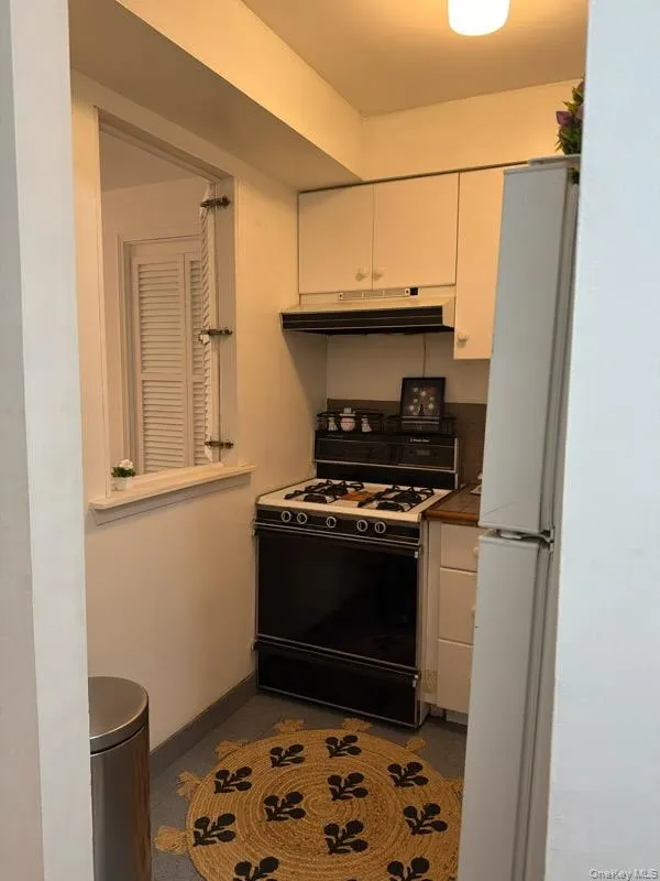 Kitchen featuring white cabinetry, range with gas cooktop, tile counters, freestanding refrigerator, and under cabinet range hood Kitchen featuring white cabinetry, range with gas cooktop, tile counters, freestanding refrigerator, and under cabinet range hood