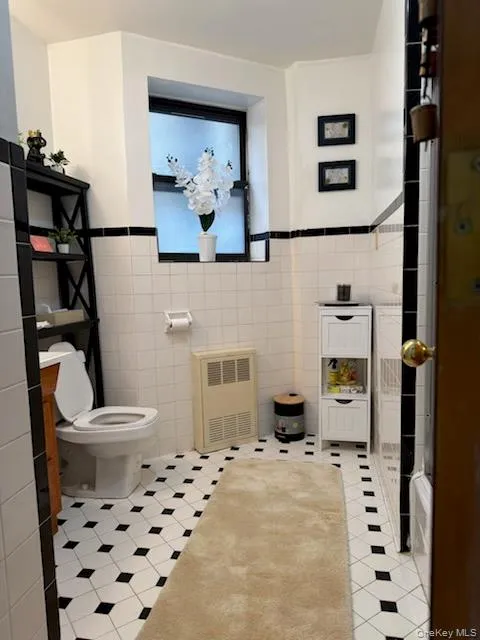 Bathroom with tile walls, radiator, a wainscoted wall, and light tile patterned floors Bathroom with tile walls, radiator, a wainscoted wall, and light tile patterned floors