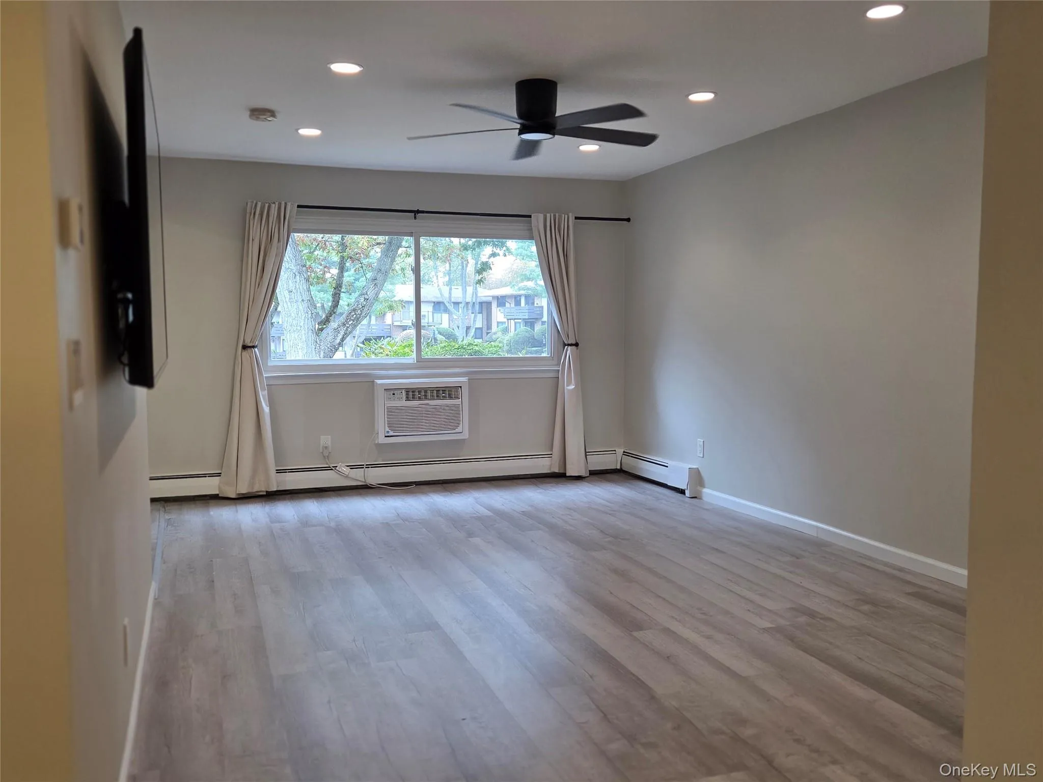 Empty room with light wood-type flooring, recessed lighting, a ceiling fan, and an AC wall unit Empty room with light wood-type flooring, recessed lighting, a ceiling fan, and an AC wall unit