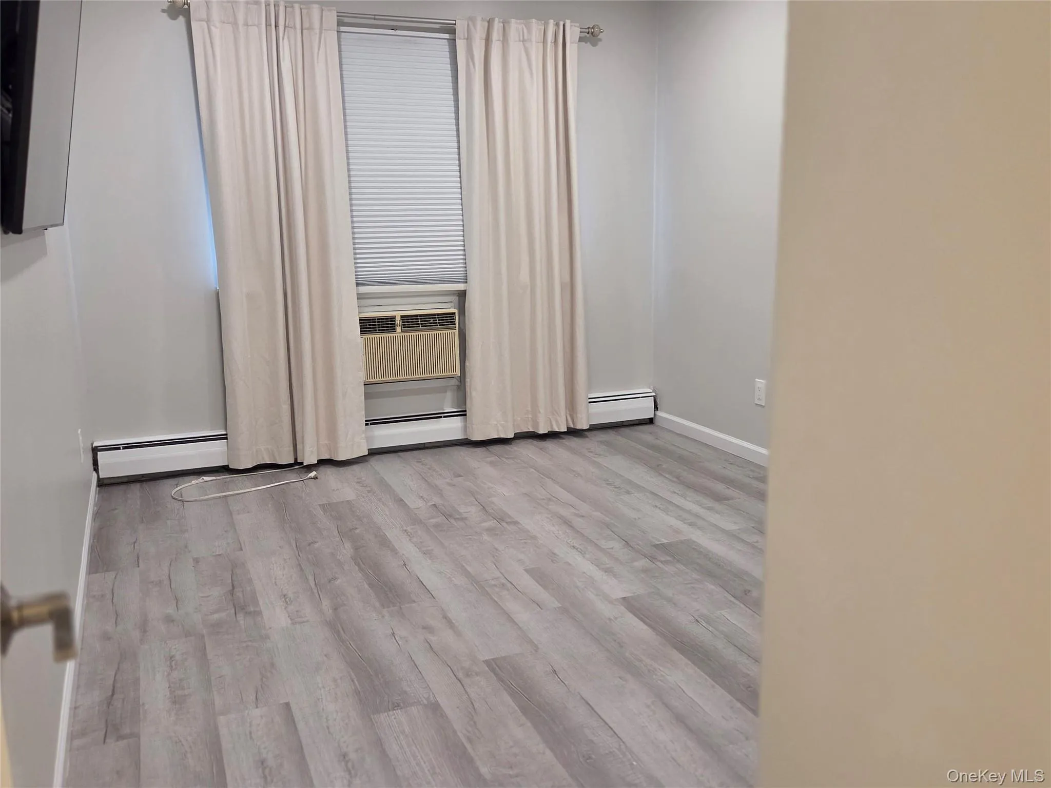 Empty room featuring light wood finished floors, cooling unit, and a baseboard heating unit Empty room featuring light wood finished floors, cooling unit, and a baseboard heating unit