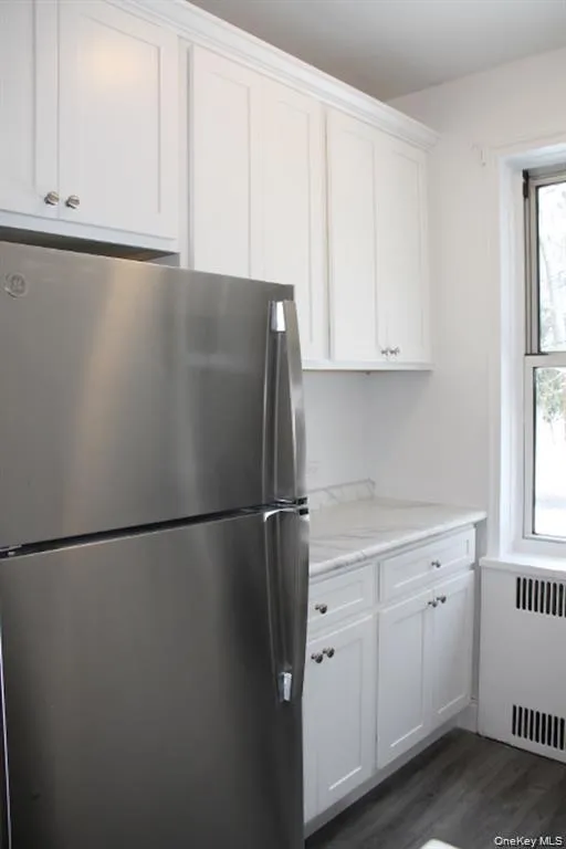 Kitchen featuring freestanding refrigerator, radiator, white cabinets, and dark wood-style flooring Kitchen featuring freestanding refrigerator, radiator, white cabinets, and dark wood-style flooring