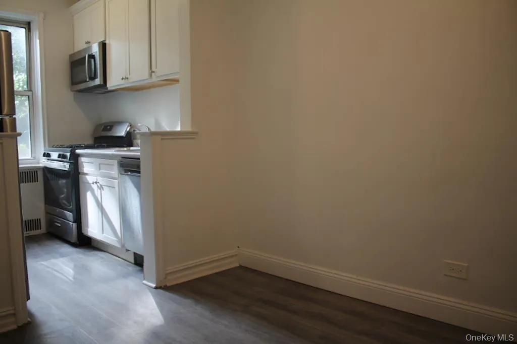 Kitchen with white cabinets, stainless steel appliances, dark wood-type flooring, radiator, and light countertops Kitchen with white cabinets, stainless steel appliances, dark wood-type flooring, radiator, and light countertops