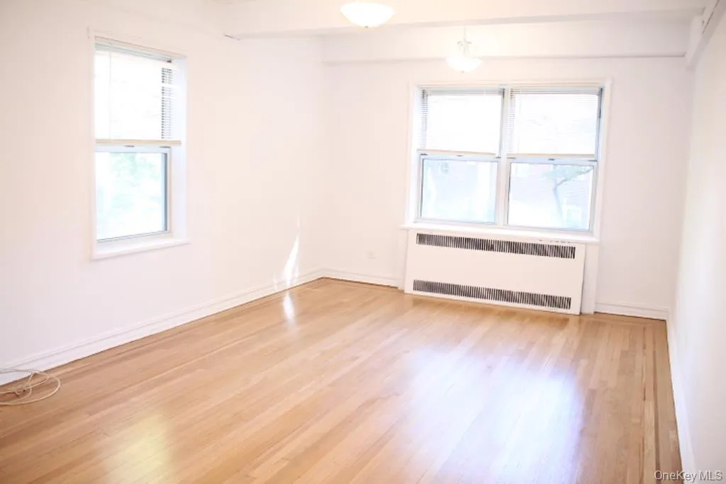 Empty room with radiator, healthy amount of natural light, and light wood-style floors Empty room with radiator, healthy amount of natural light, and light wood-style floors