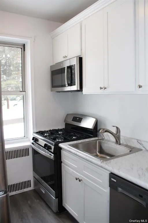 Kitchen with appliances with stainless steel finishes, radiator, light countertops, white cabinetry, and dark wood finished floors Kitchen with appliances with stainless steel finishes, radiator, light countertops, white cabinetry, and dark wood finished floors