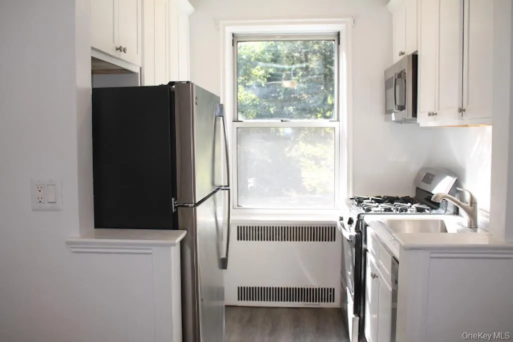 Kitchen with white cabinetry, stainless steel appliances, radiator heating unit, and light wood-type flooring Kitchen with white cabinetry, stainless steel appliances, radiator heating unit, and light wood-type flooring