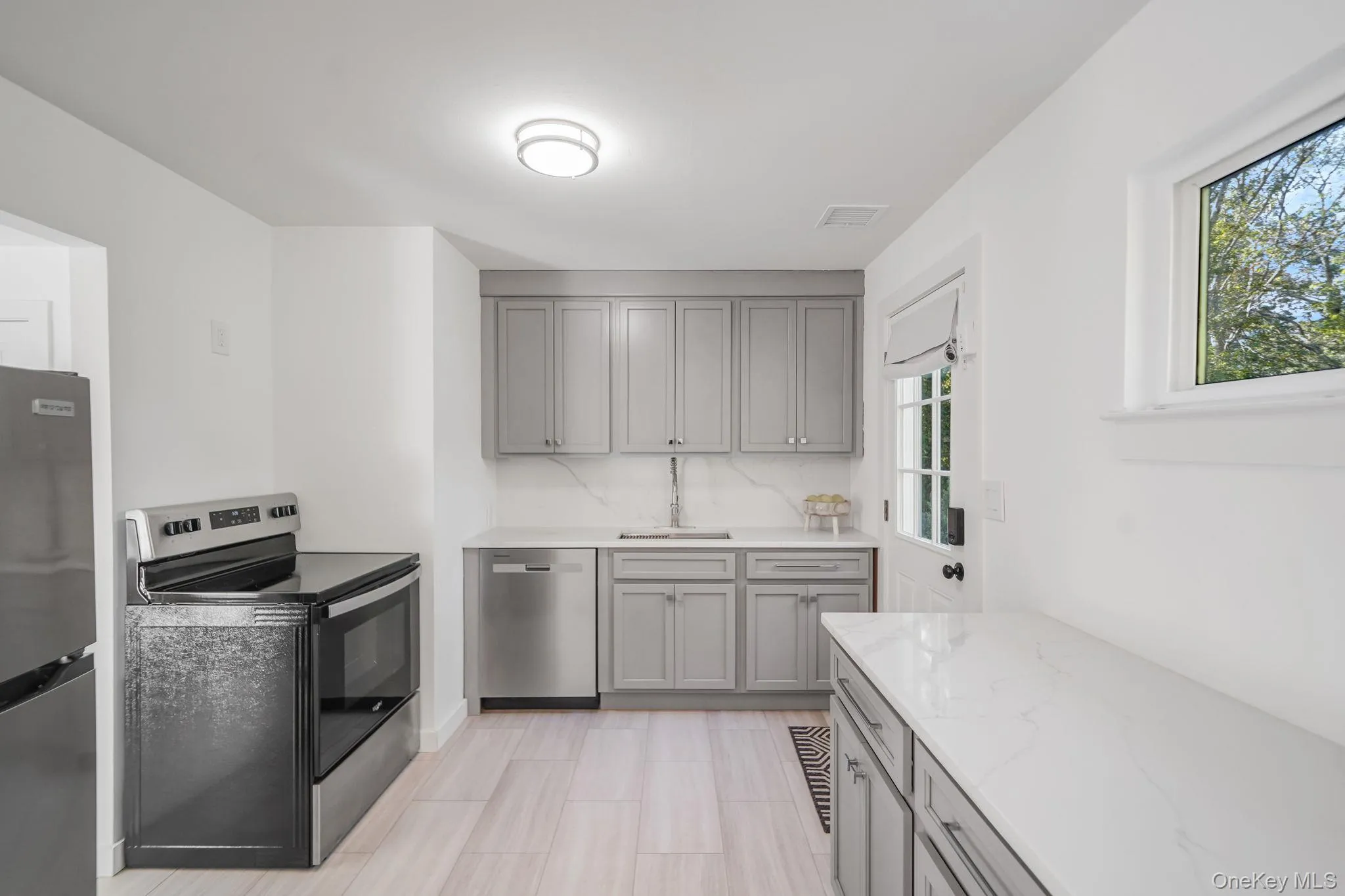 Kitchen with gray cabinetry, appliances with stainless steel finishes, light stone counters, and tasteful backsplash Kitchen with gray cabinetry, appliances with stainless steel finishes, light stone counters, and tasteful backsplash